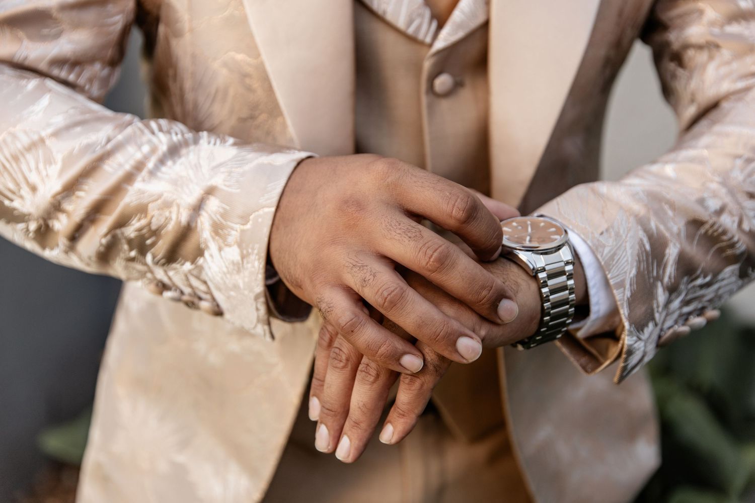 Close up of hands wearing elegant gold and beige formal attire with a silver watch visible.