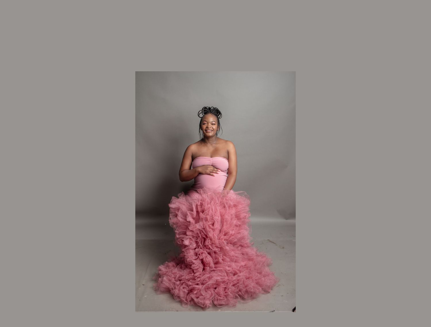 Portrait in a pink ruffled formal gown against a grey backdrop.