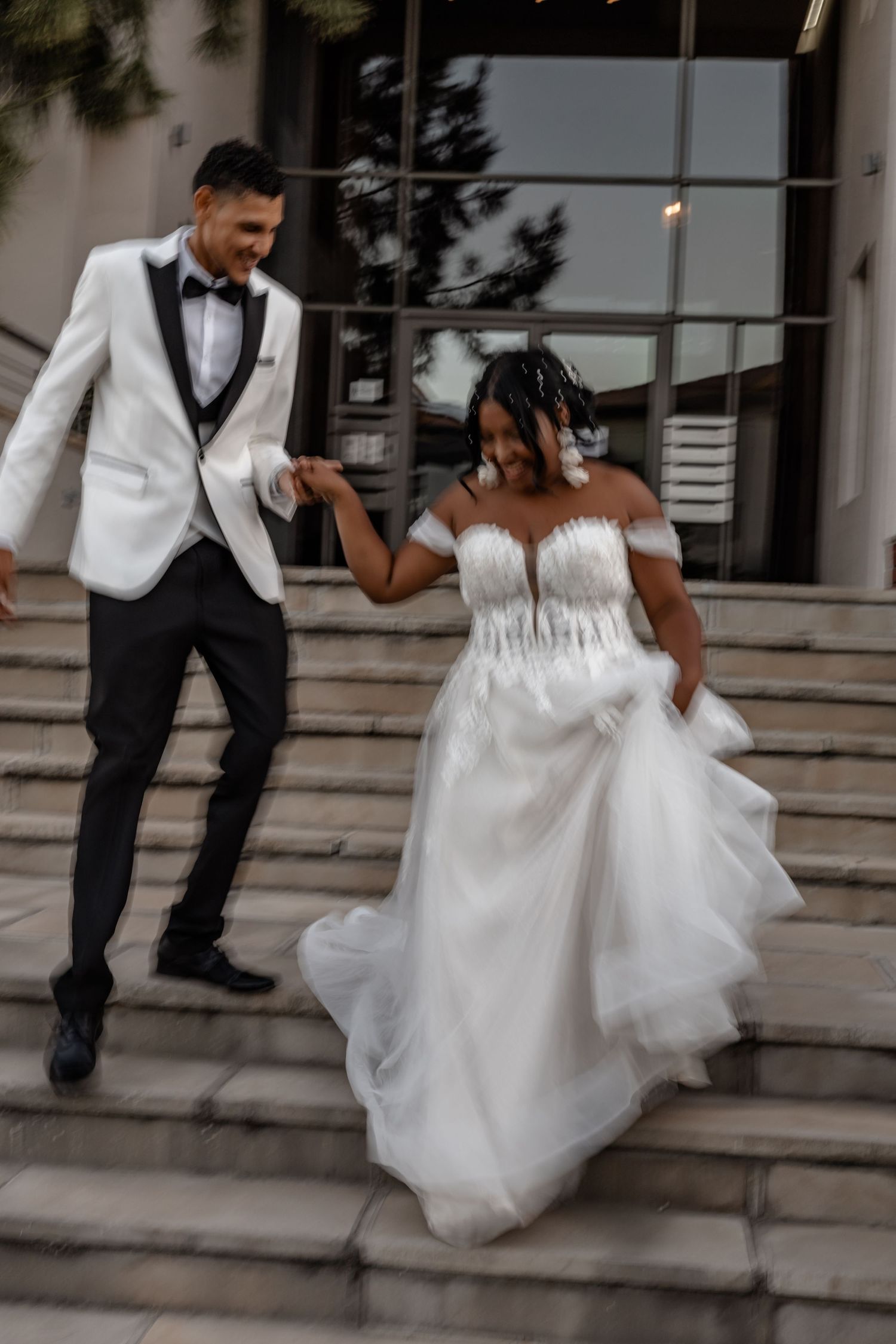 Wedding couple playfully descending outdoor stone steps in formal attire.