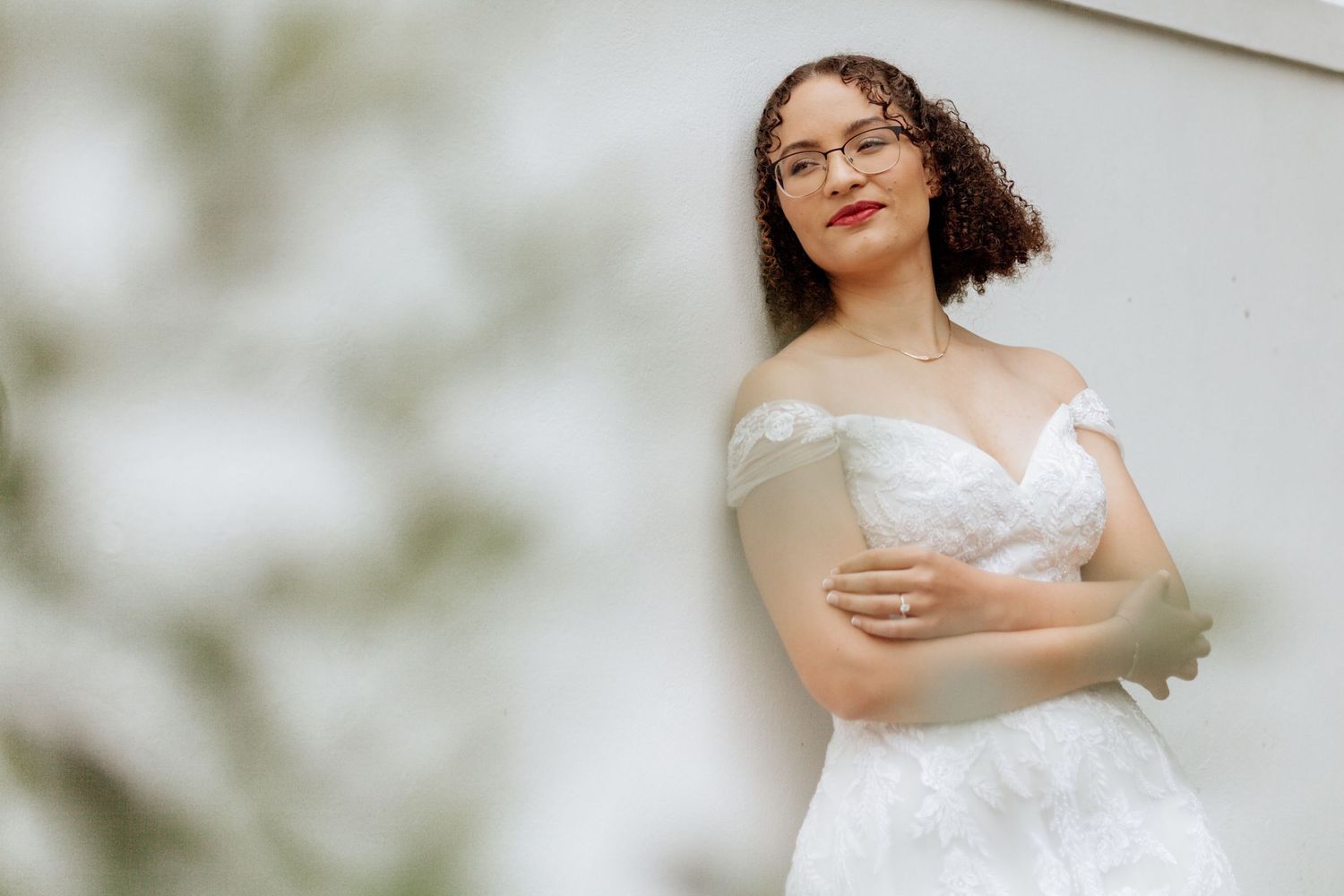 A bride in a delicate white off-shoulder wedding gown poses gracefully against a soft, light background.