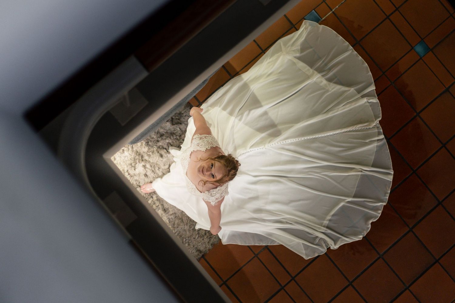 Aerial view of a bride in a white wedding gown with a full skirt, standing on a tiled floor.