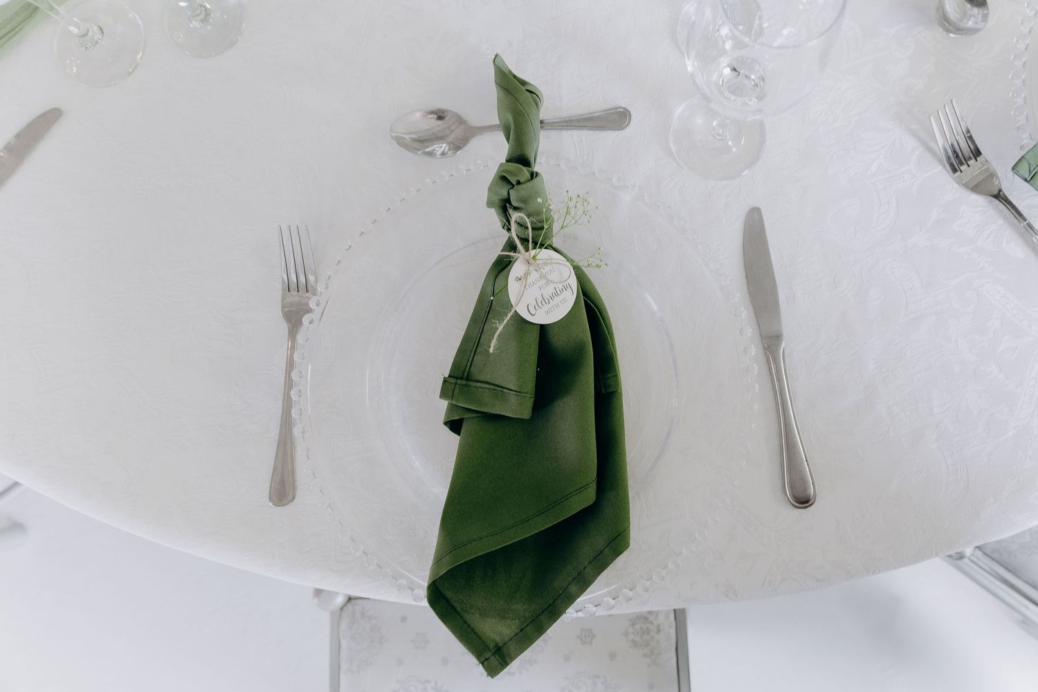 A formal dining table setting with white tablecloth, green napkins, and elegant silverware arranged for a special occasion.