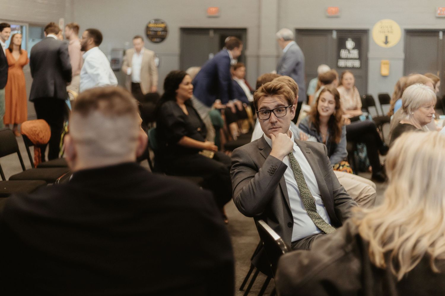 A crowded indoor event space with people mingling and networking at tables during a professional gathering.