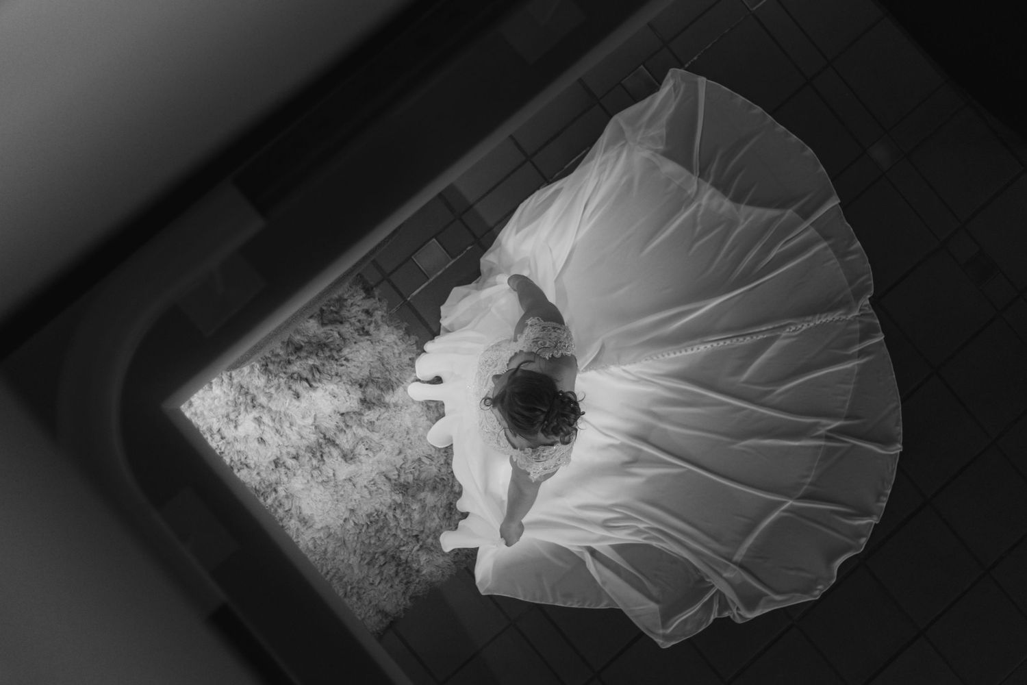 Black and white aerial photo of a bride in a flowing white wedding dress standing in a doorway.