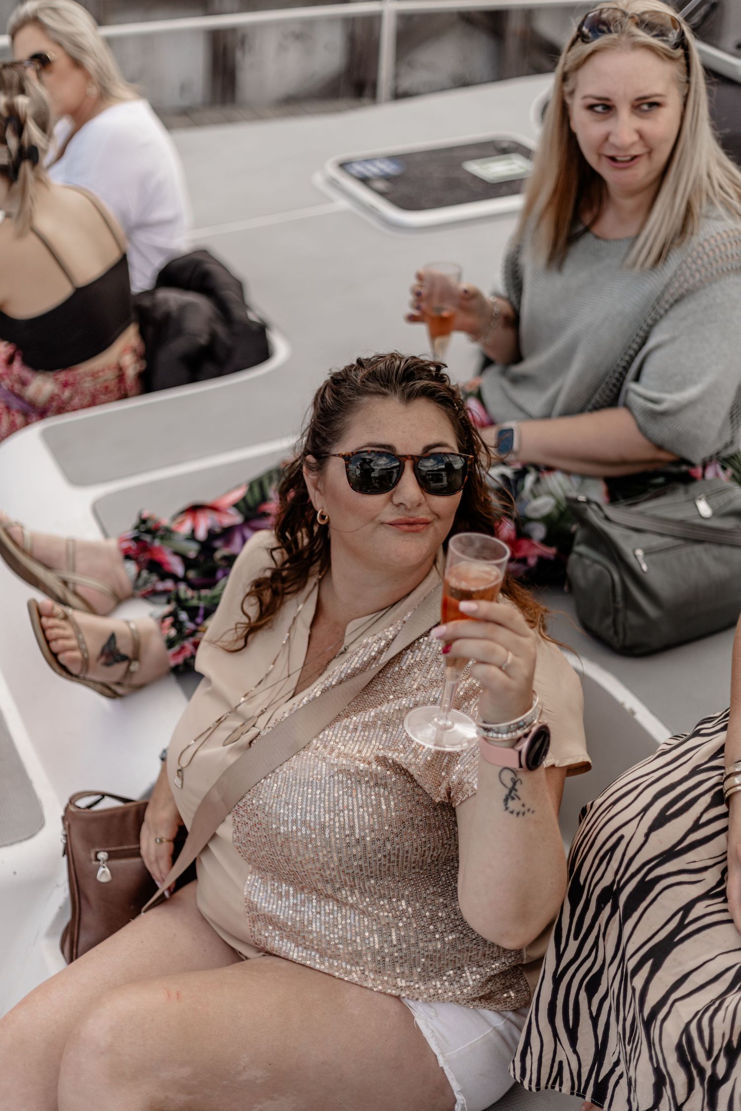 Group enjoying drinks and conversation on a boat deck wearing sunglasses and sparkly outfits.