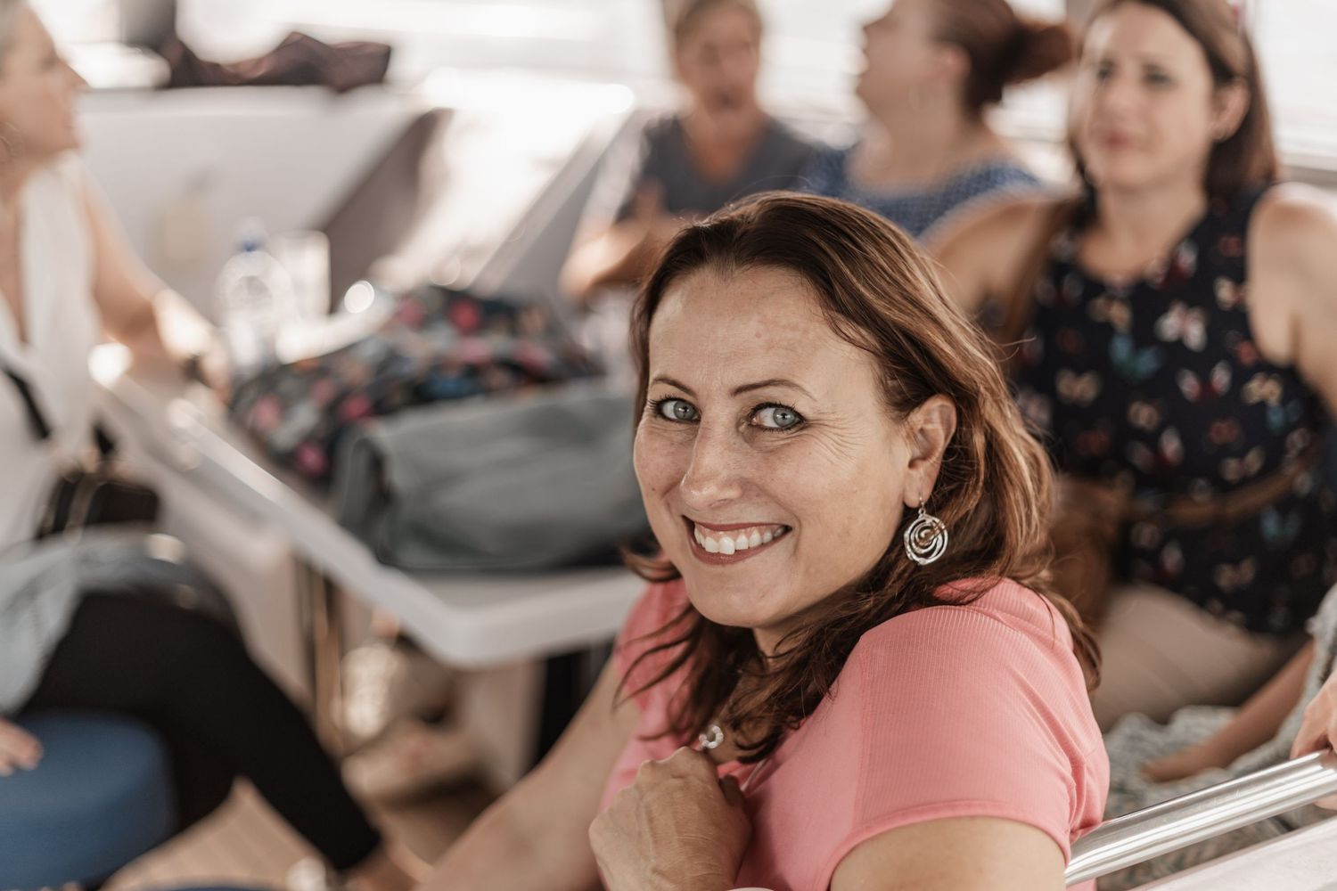 Woman in pink shirt sits smiling amongst fellow passengers in what appears to be public transportation.