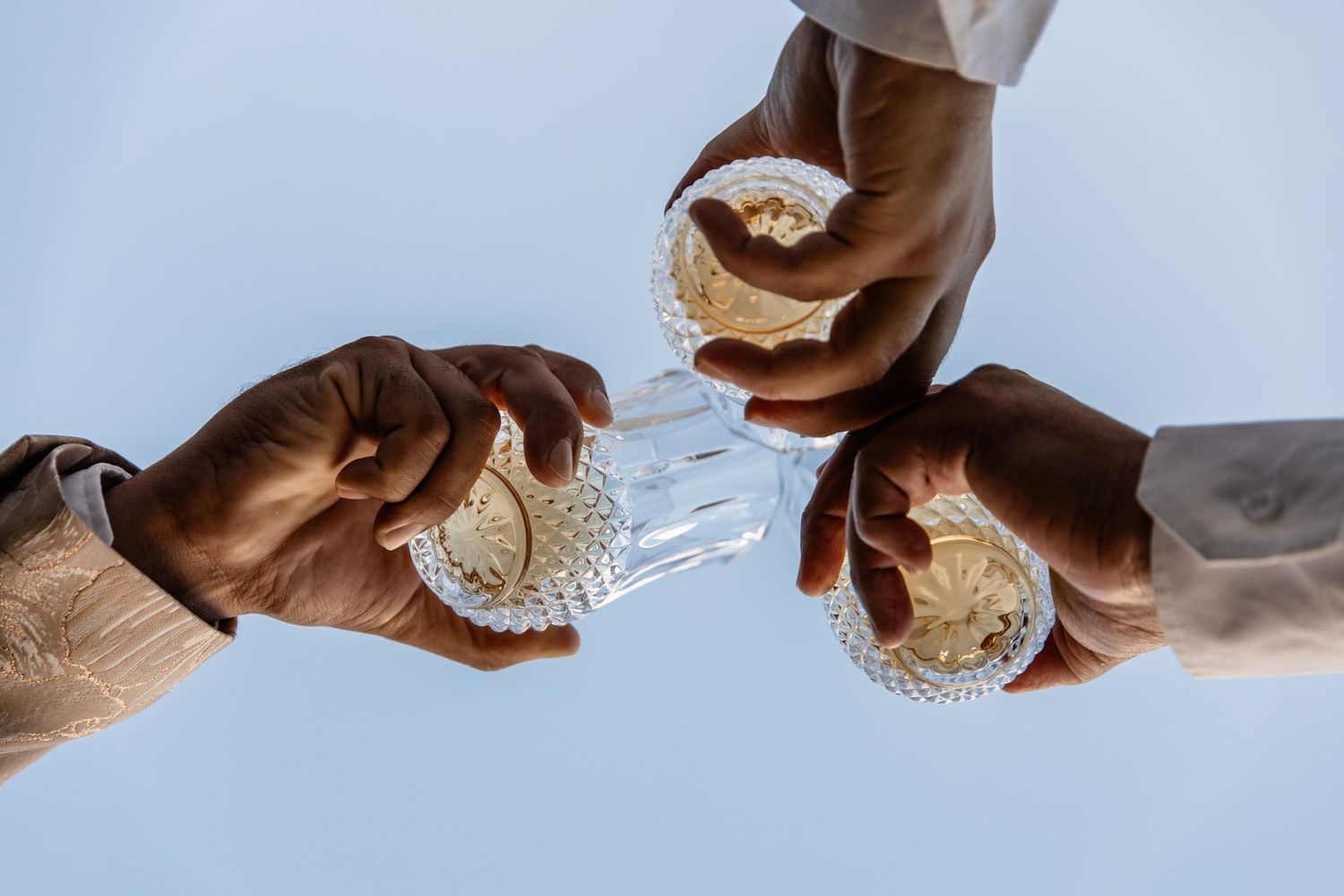 Several hands reach toward the center holding white paper cups against a light blue background.