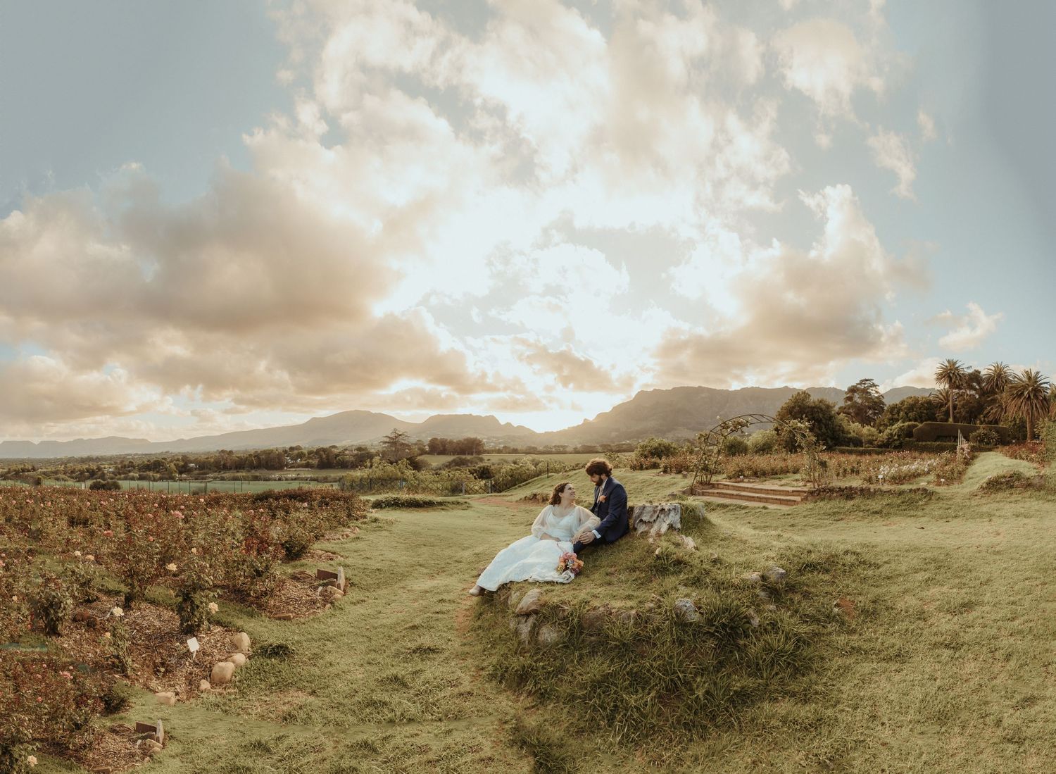 A panoramic view of rolling green hills under dramatic cloudy skies with a distant mountain landscape.