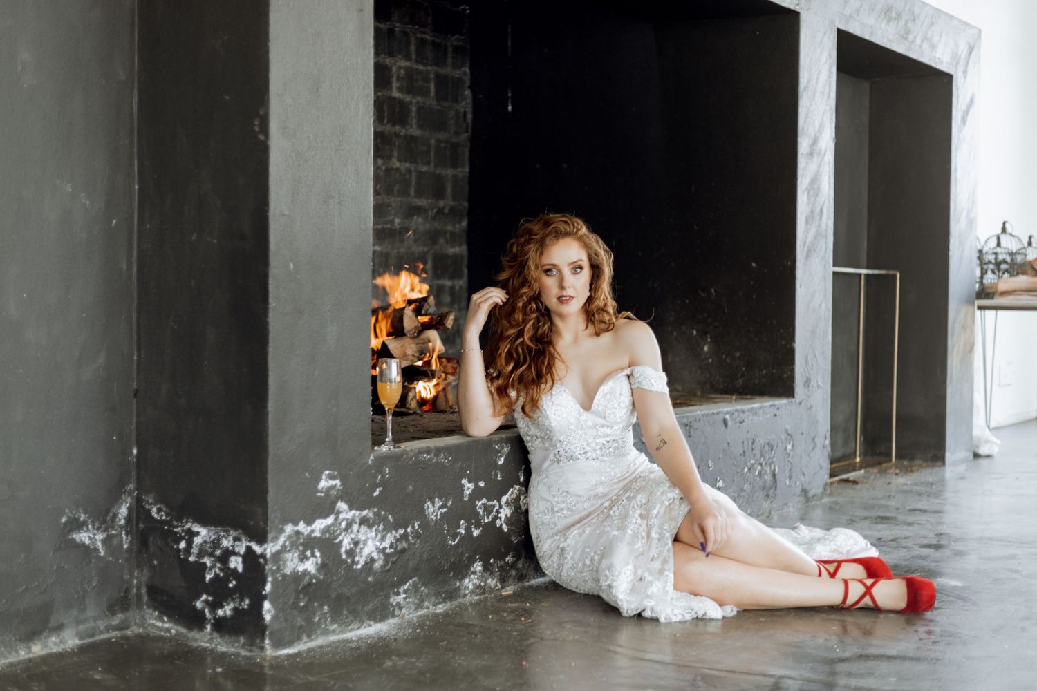 A bride in a white lace wedding dress reclines on a concrete floor against an industrial gray wall.