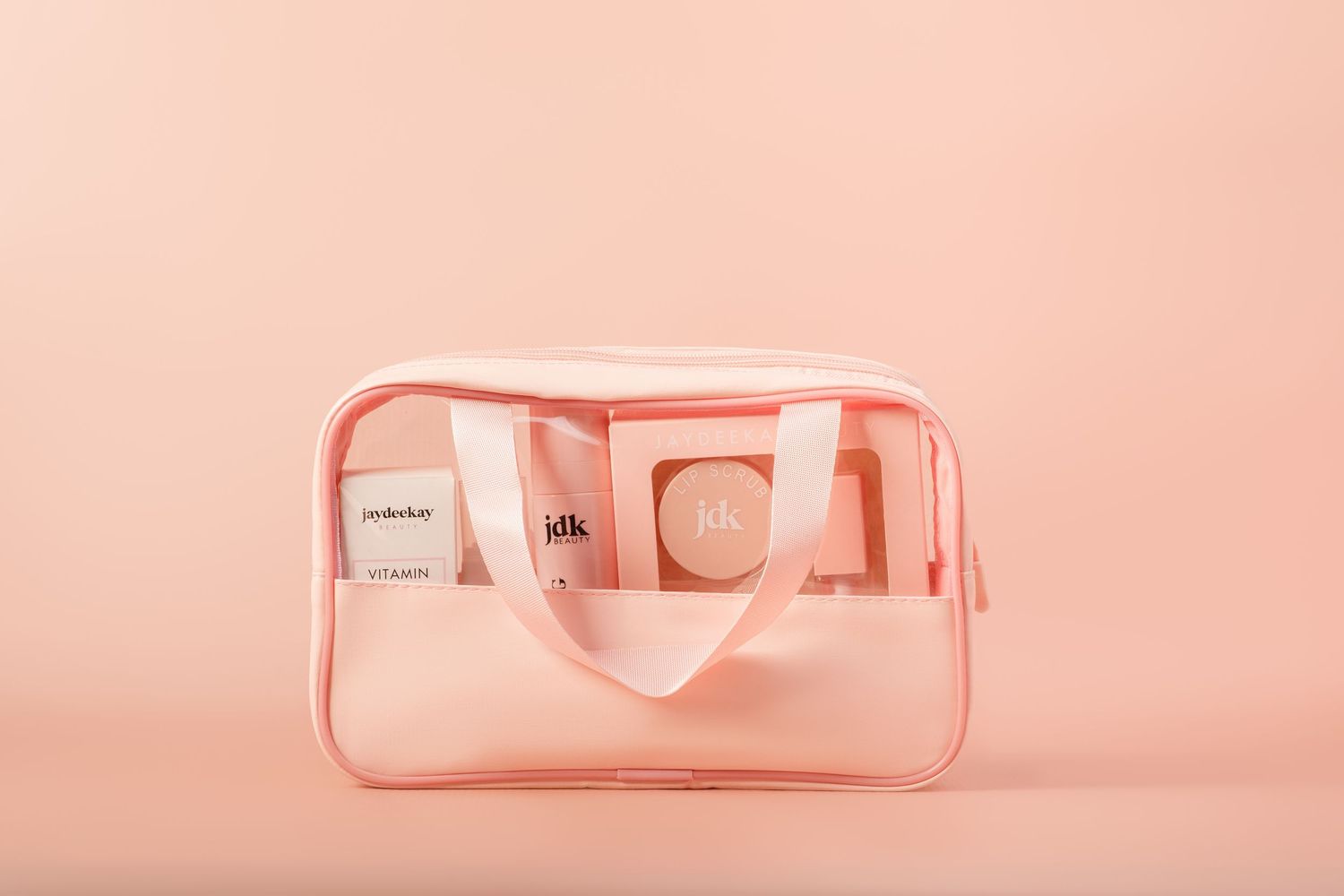 Pink beauty products and cosmetics arranged in a monochromatic display against a soft coral background.
