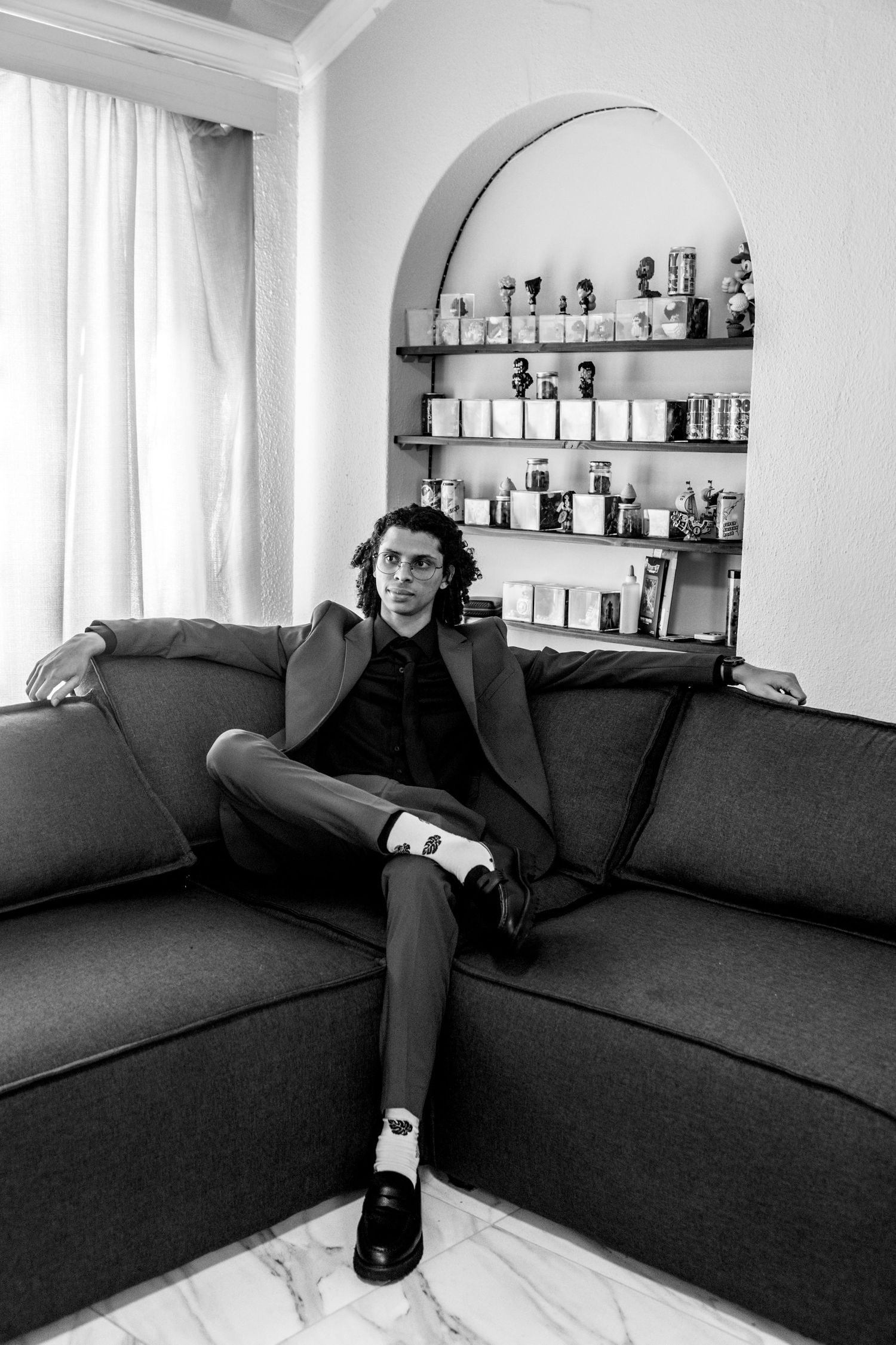 A sequence of black and white photos showing a person lounging and posing with dramatic shadows on a dark couch.