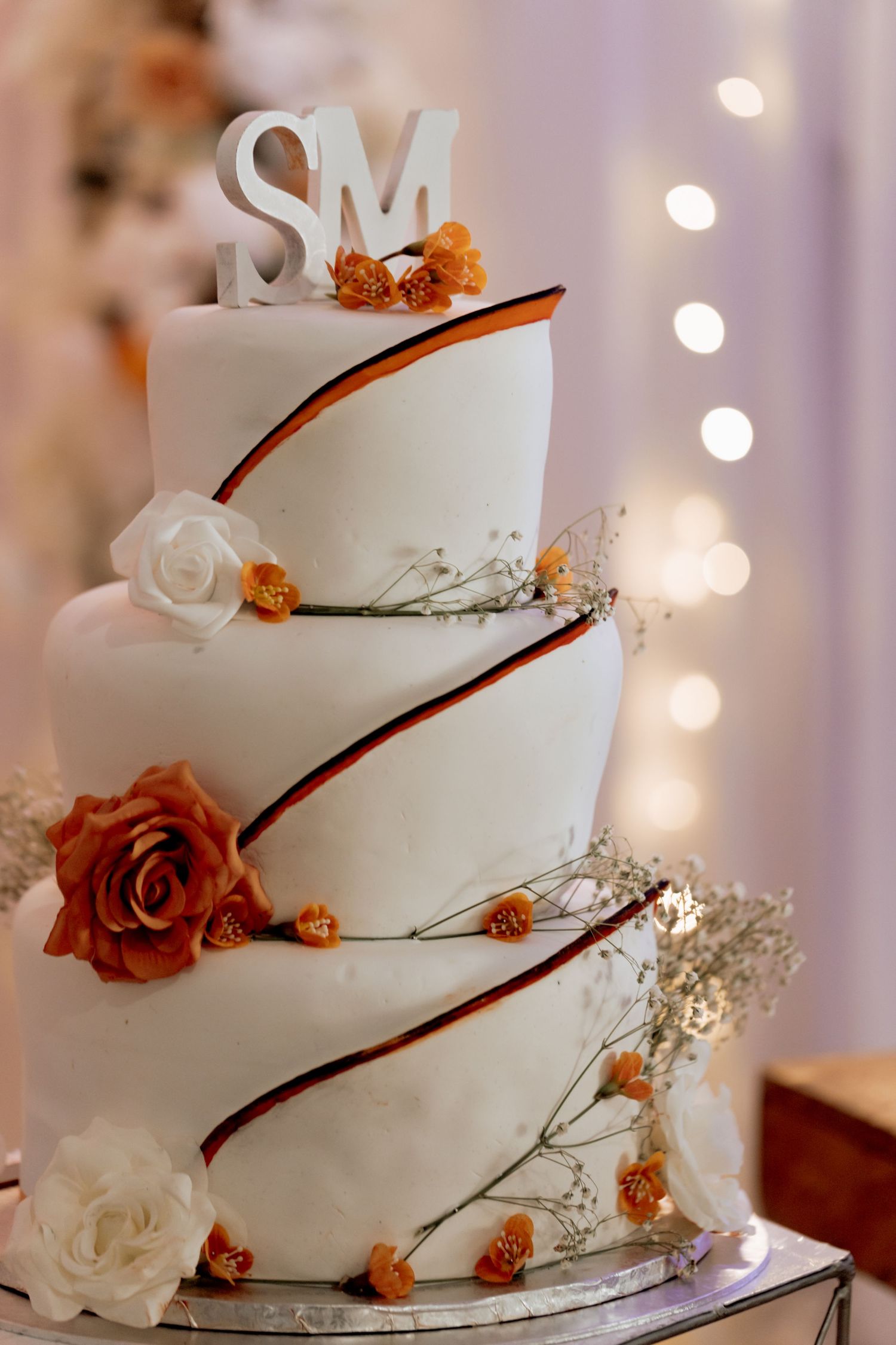 Elegant three-tiered white wedding cake decorated with orange and white roses, branches, and white Mr and Mrs topper.