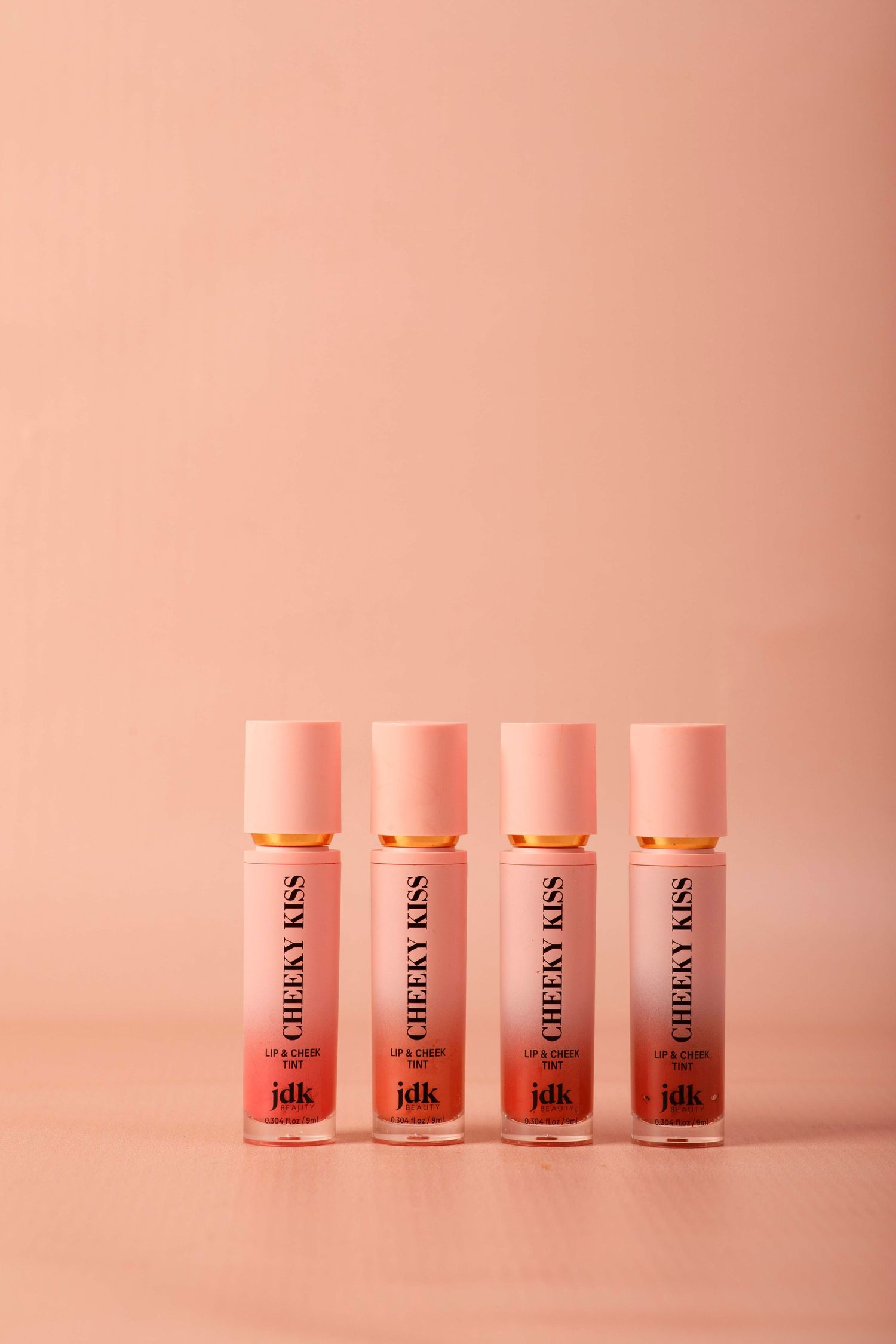 Four small pink glass jars with black text arranged in a minimalist composition against a pink background.