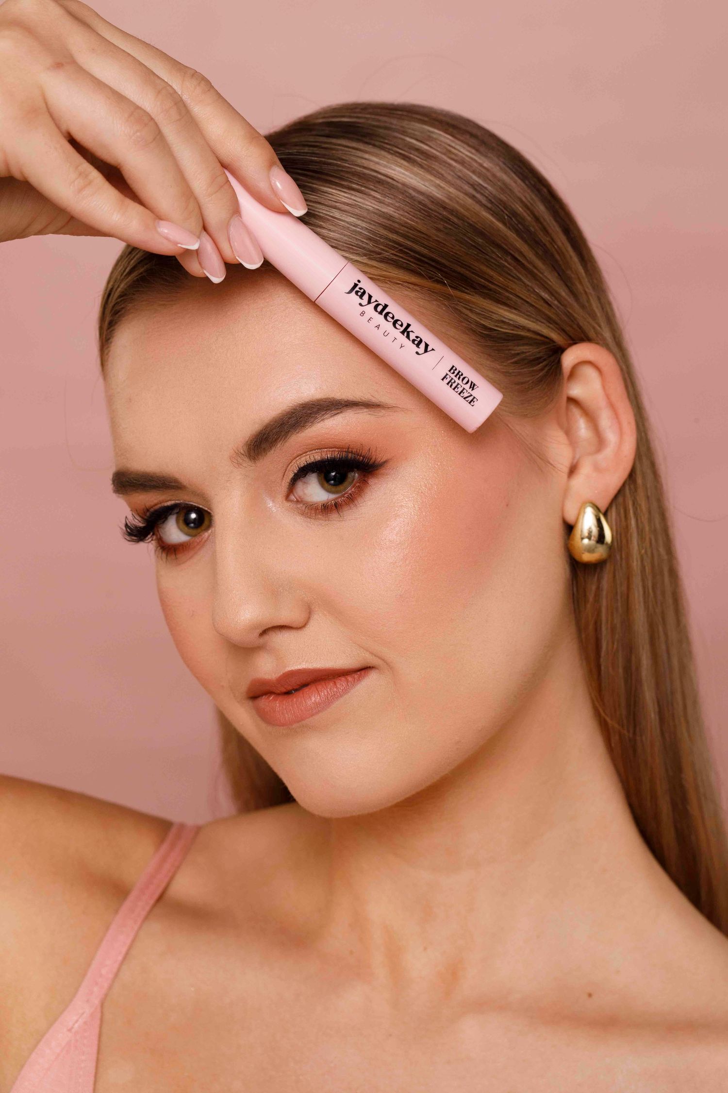 Beauty product being applied to model's face against pink background in makeup application demonstration series.
