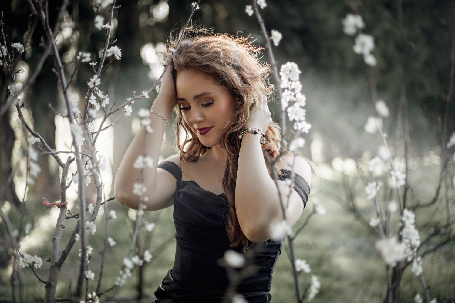 Dark romantic portrait amidst flowering tree branches in moody forest lighting.