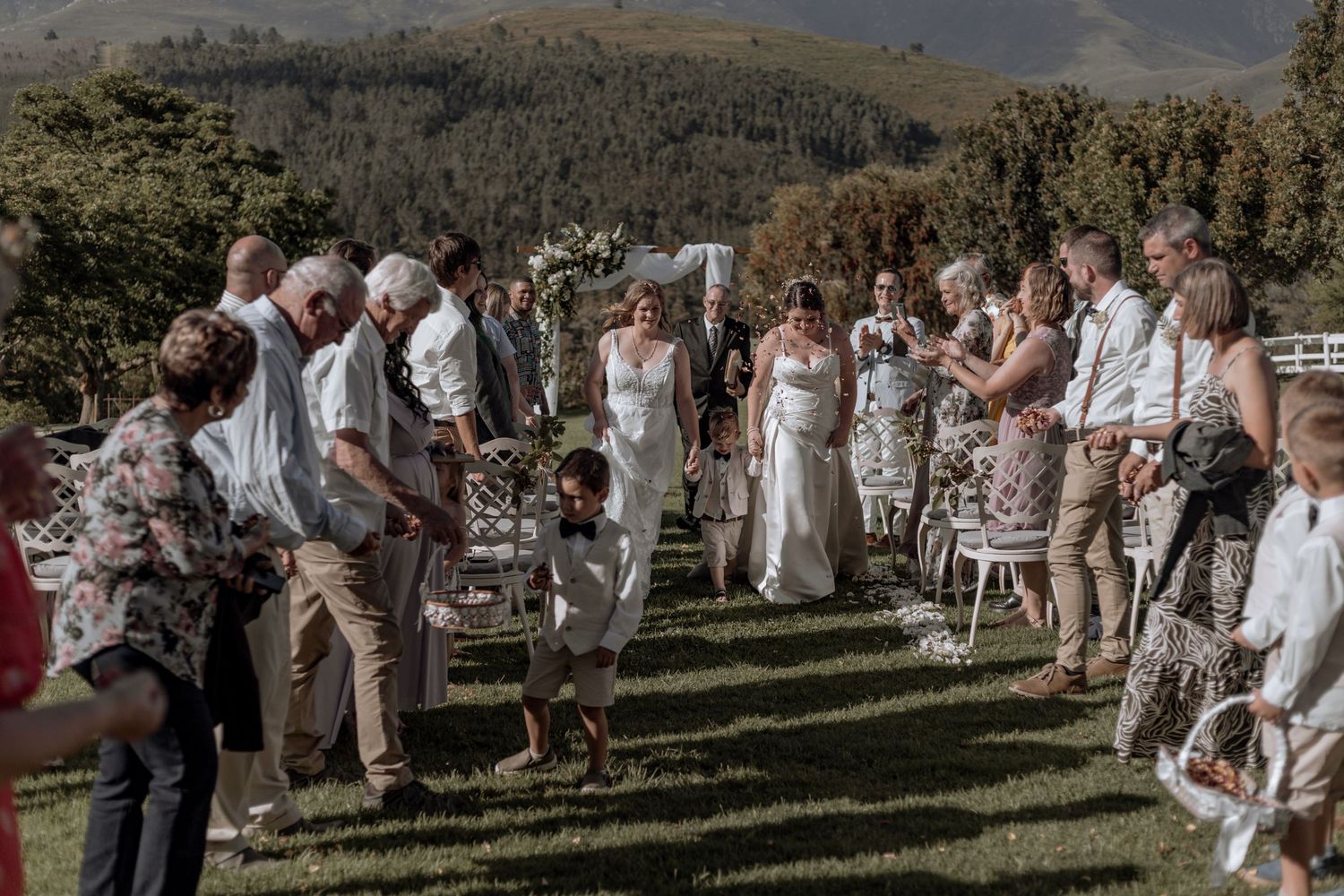 Wedding guests dance outdoors on a rustic patio surrounded by mountains during a joyful celebration.