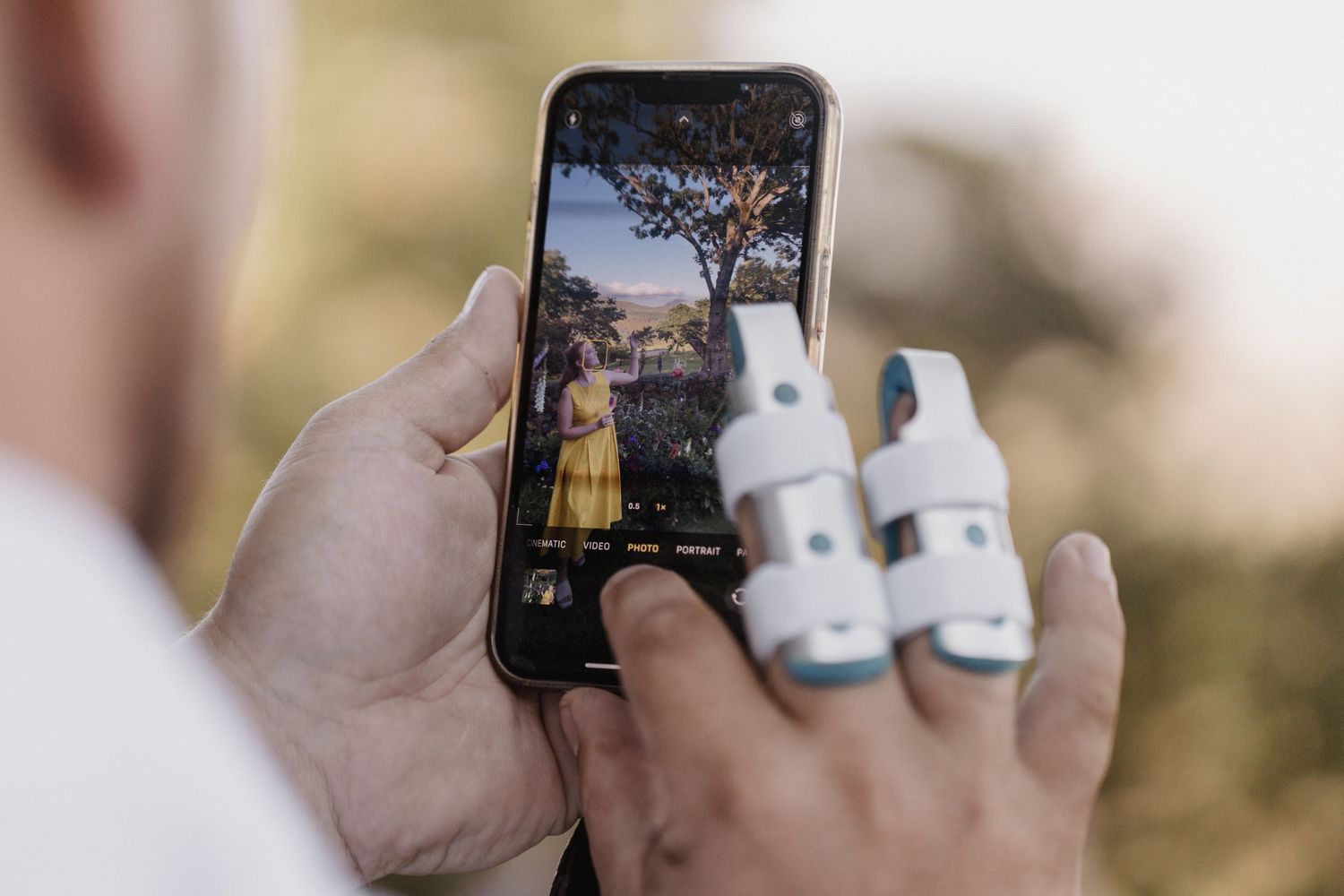Person holding a mobile phone displaying scenic nature photo while holding two small white bottles.