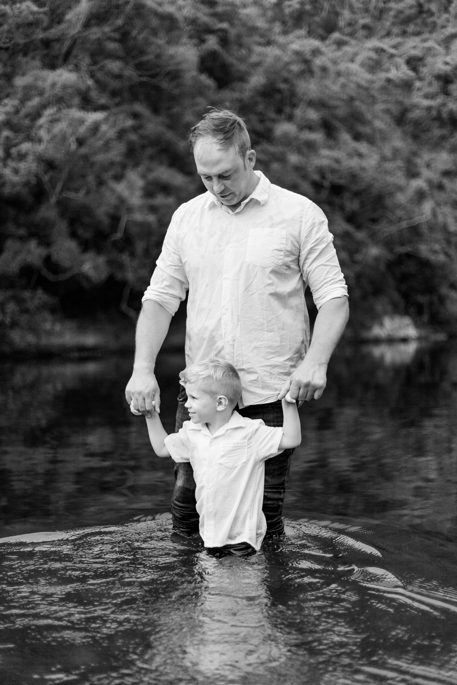 A black and white photo series shows baptism ritual being performed in a lake as two figures stand in the water together.