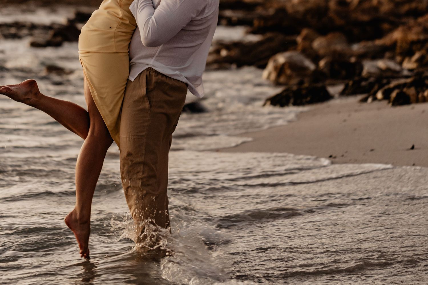 Two people standing in shallow ocean water at sunset splashing and playing along the shoreline of a beach.