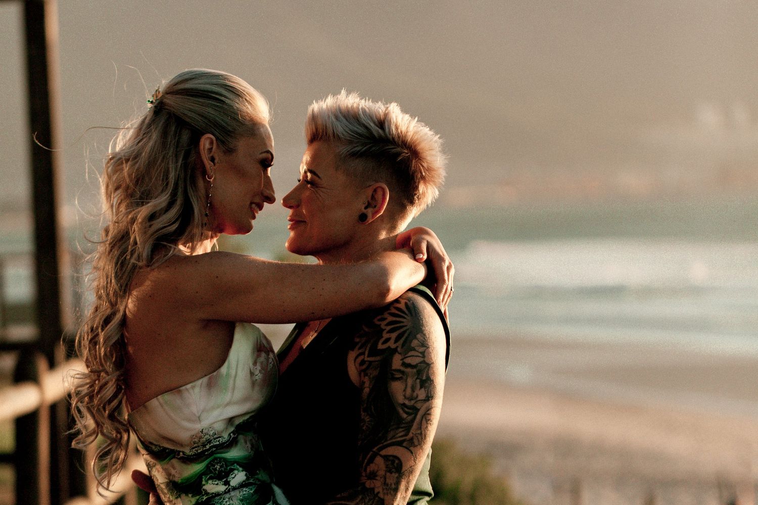 Romantic couple embraces and kisses at sunset on a beach with golden light illuminating their silhouettes.