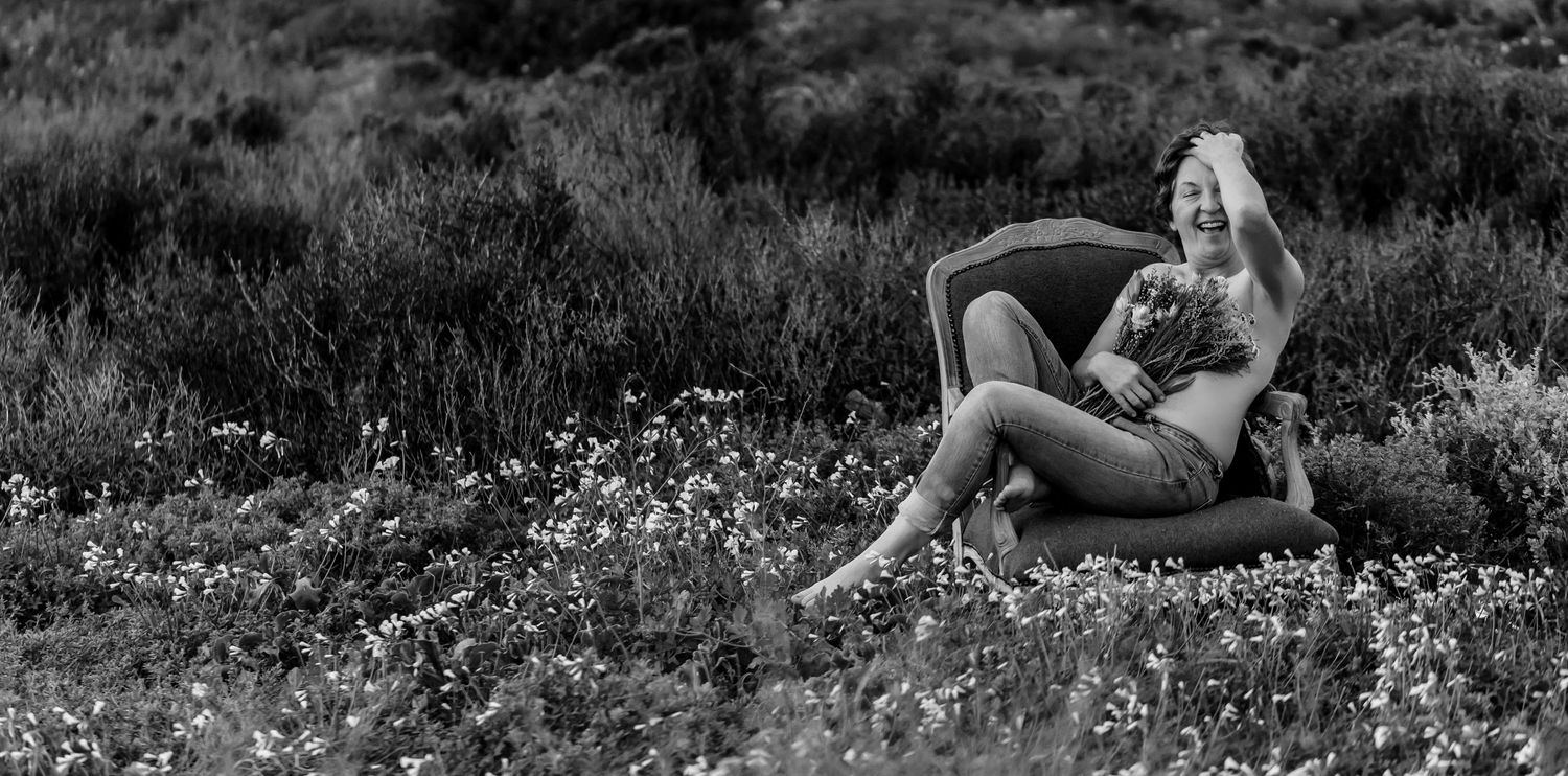 Woman in white summer dress lying down in nature surrounded by wildflowers on a sunny afternoon.