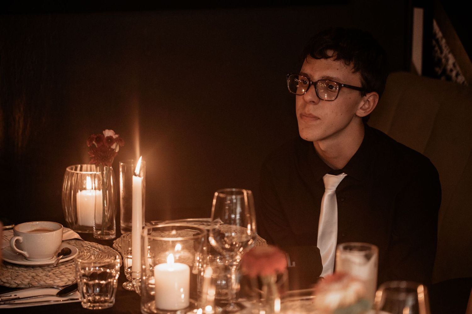 A romantic candlelit table setting with glowing candles and white tablecloths in a dimly lit restaurant atmosphere.