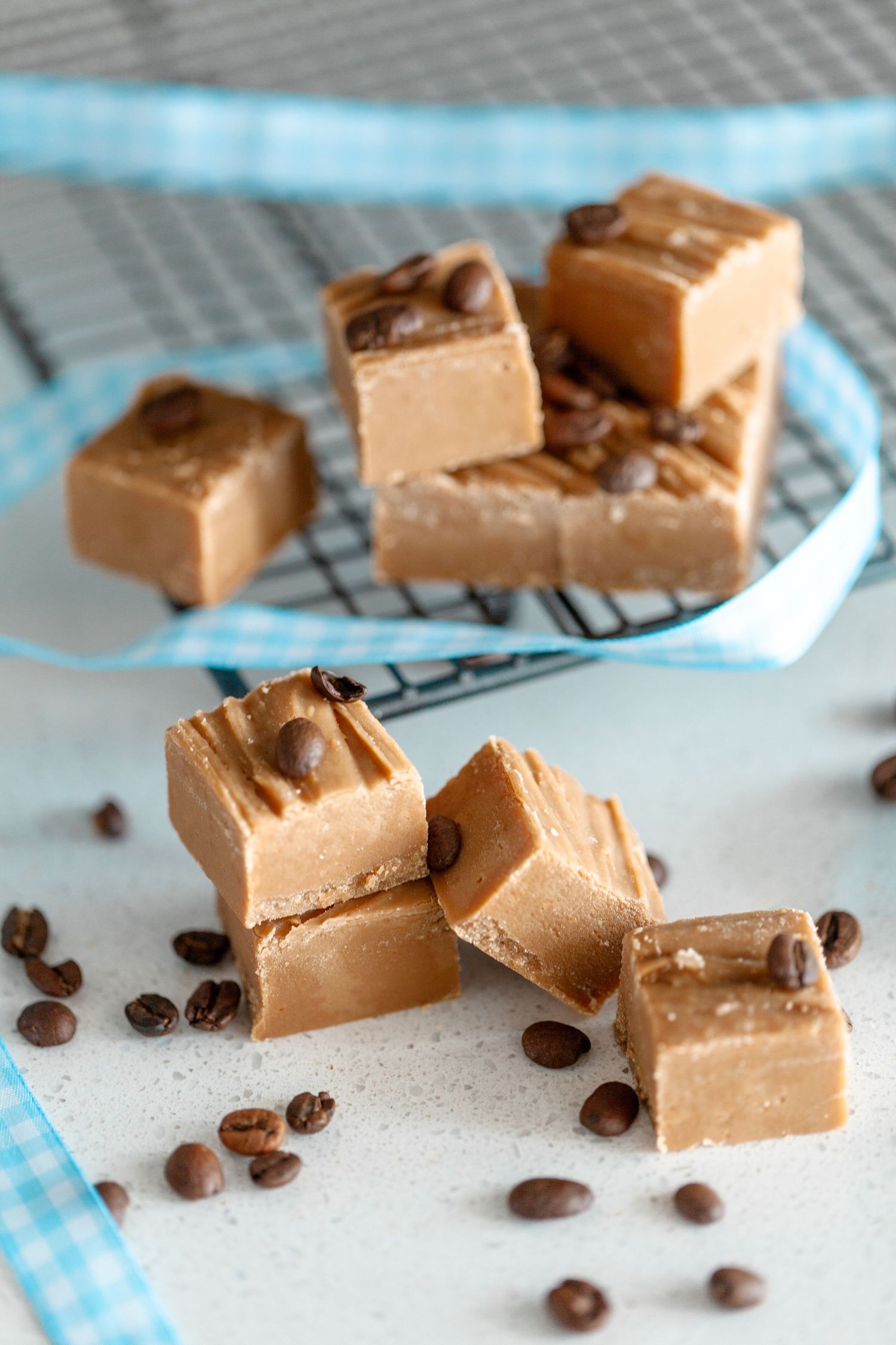 Homemade coffee fudge squares scattered with roasted coffee beans on a blue and white checkered napkin.