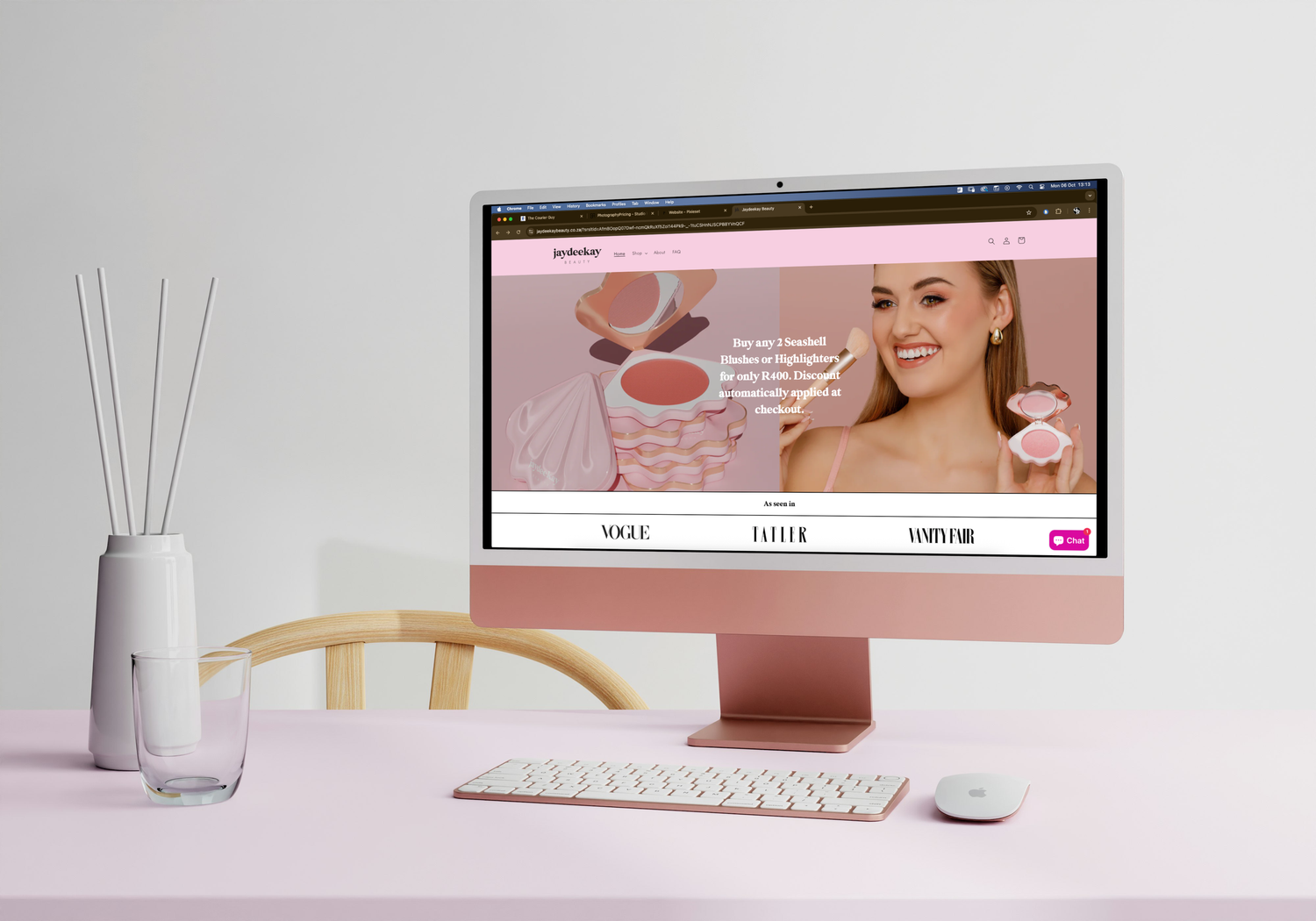 Minimalist pink workspace setup with computer monitor, keyboard, mouse and reed diffuser on white desk surface.