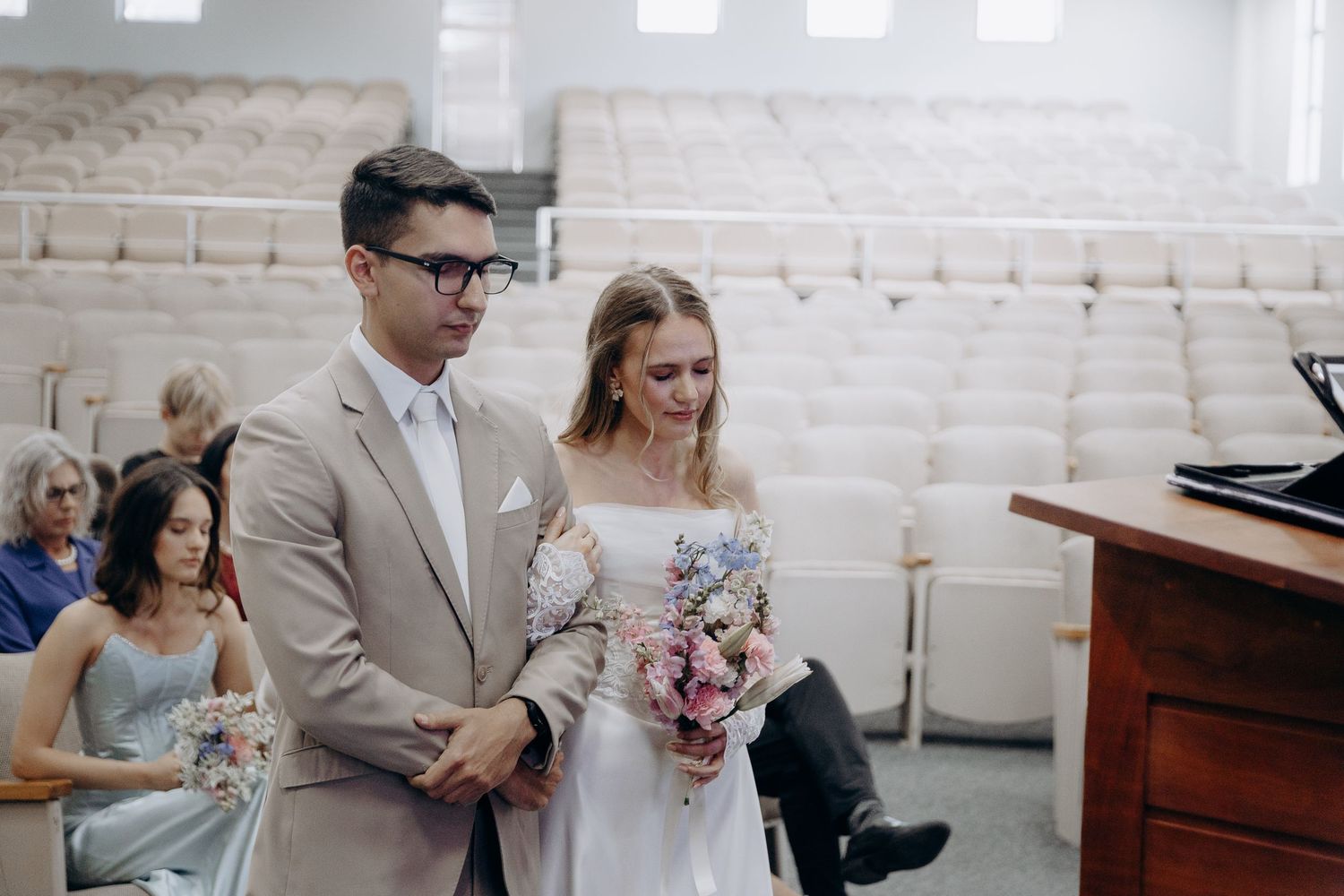 Elegant wedding ceremony in a rustic white brick venue with natural lighting streaming through windows.