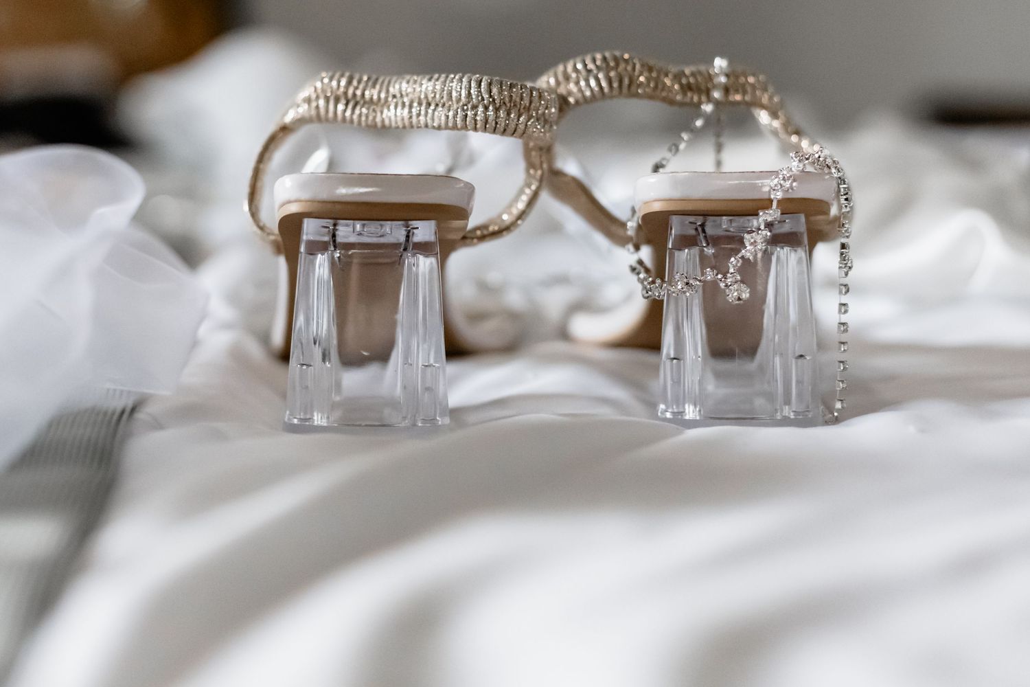 A pair of elegant crystal and silver bridal sandals resting on white fabric.
