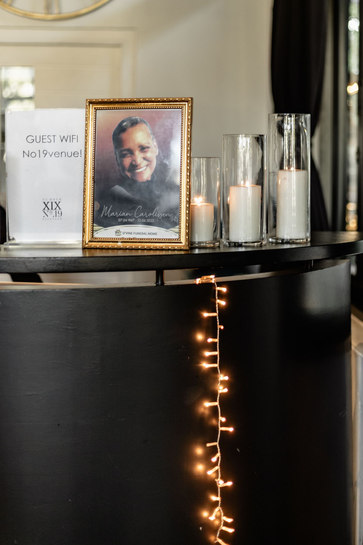 Decorative table display with a framed photo, candles in glass holders, and string lights glowing on black furniture.