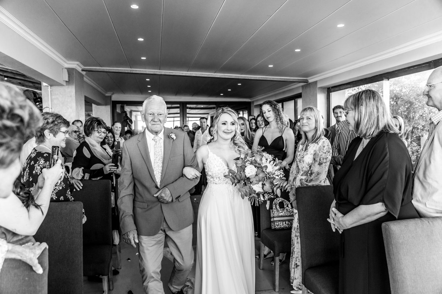 Black and white photo of a joyful wedding ceremony entrance with guests lining the aisle while couple walks through.
