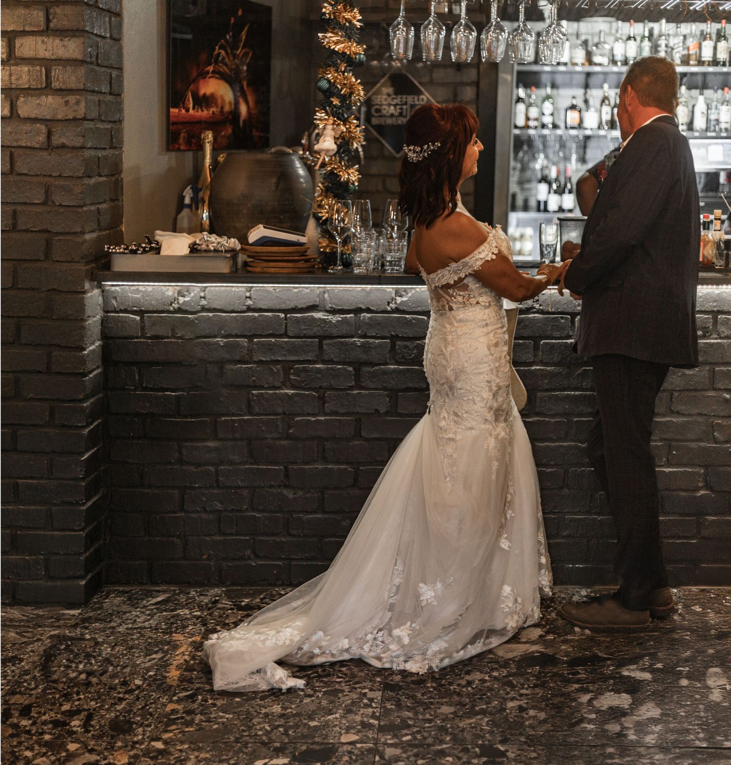 A bride and groom dance together in front of a rustic brick wall at an indoor venue with romantic lighting.