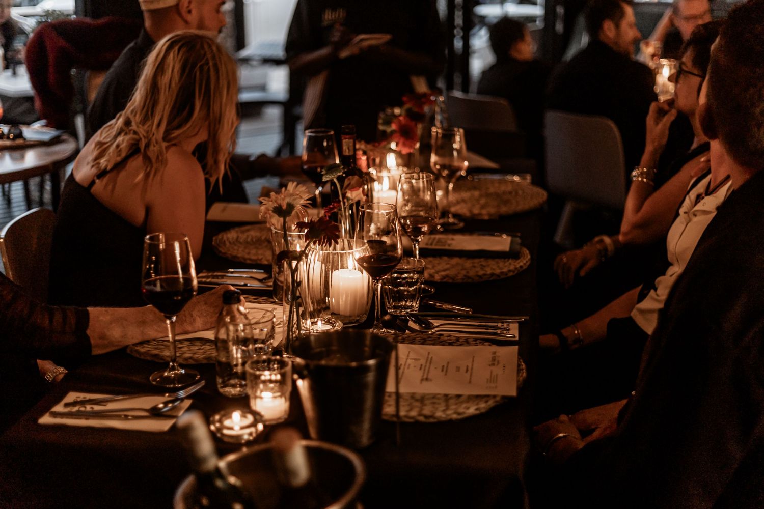 Candlelit dinner table set with wine glasses and place settings creates an intimate ambiance in a dimly lit restaurant.