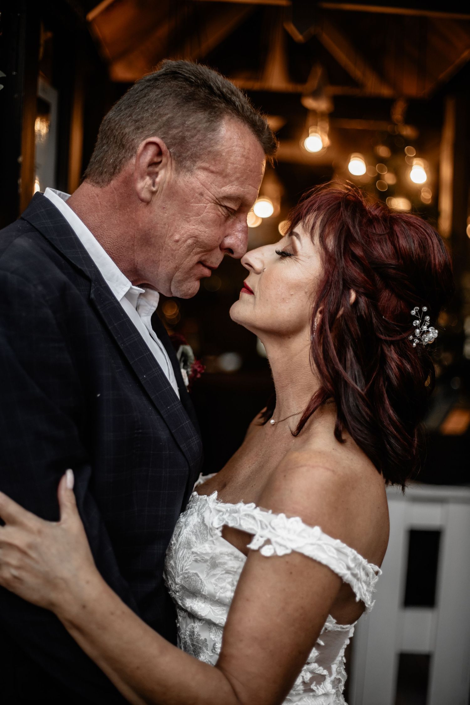 A couple shares an intimate moment in dim lighting at their wedding reception as they embrace on the dance floor.
