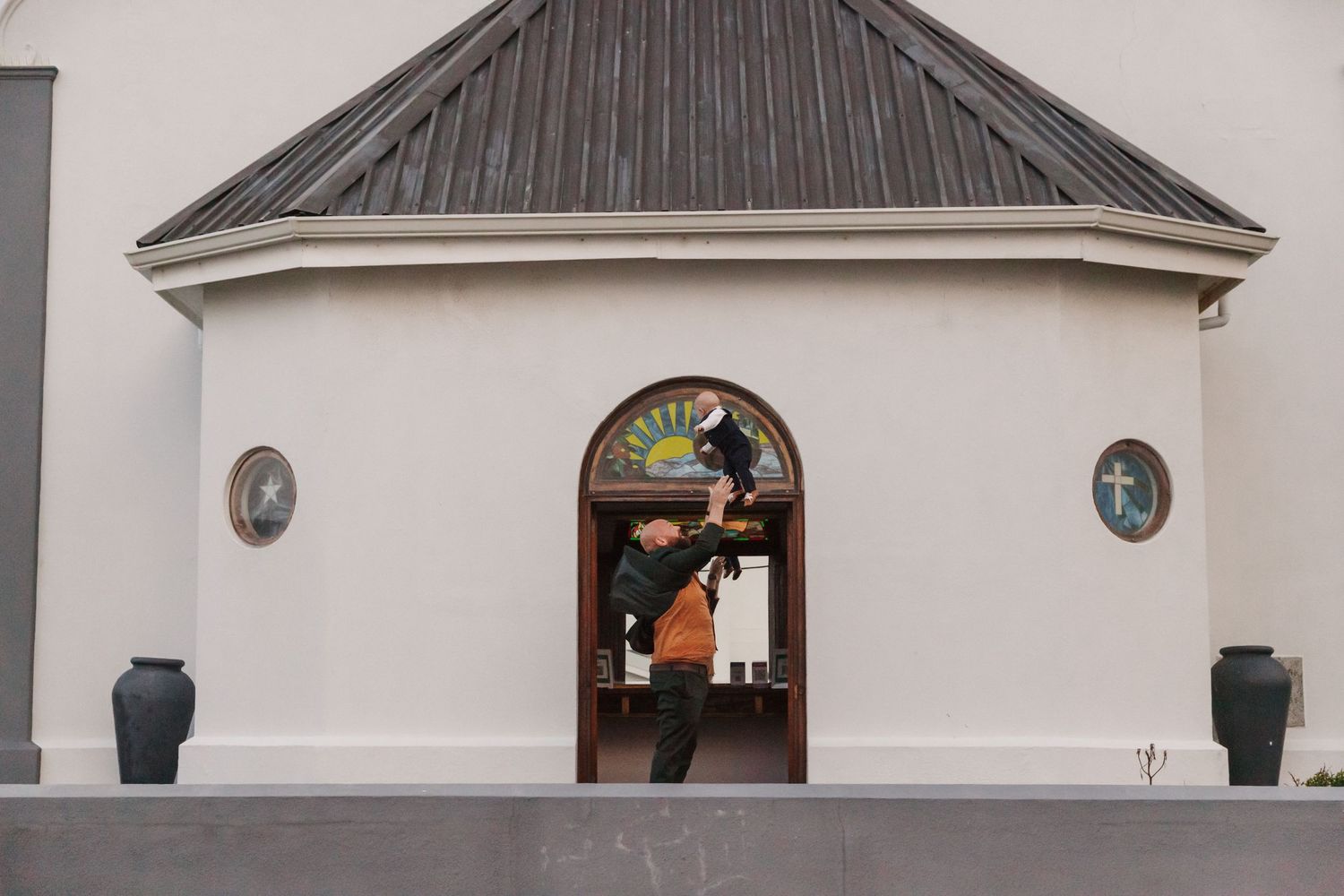 Person entering an arched doorway of a white church building with stained glass and a cross symbol.