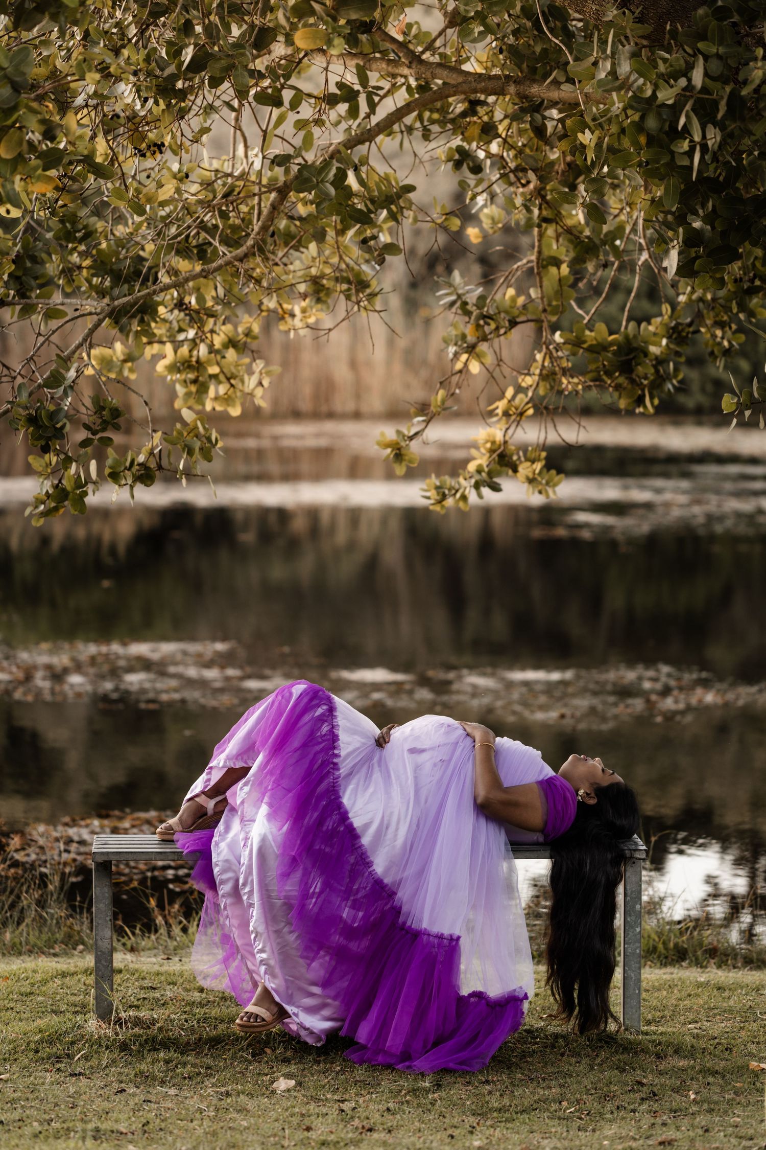 A purple and white layered tulle dress creates a dreamy silhouette against a natural outdoor backdrop by a lake.
