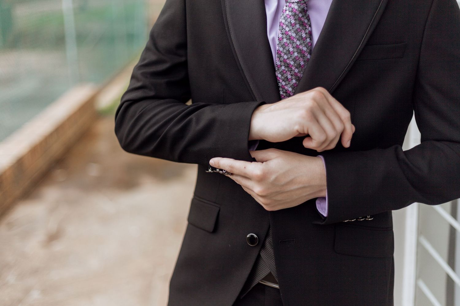 Professional in a black suit and purple tie holds a mobile phone while standing in an elegant setting.