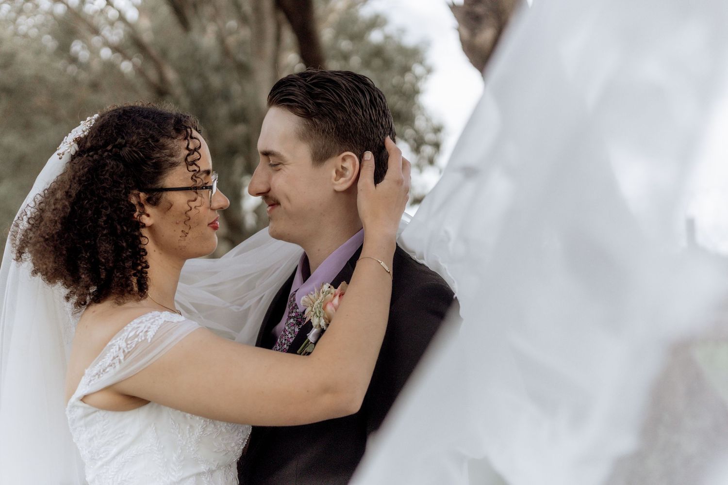 Wedding couple in intimate embrace surrounded by natural outdoor scenery and soft light.