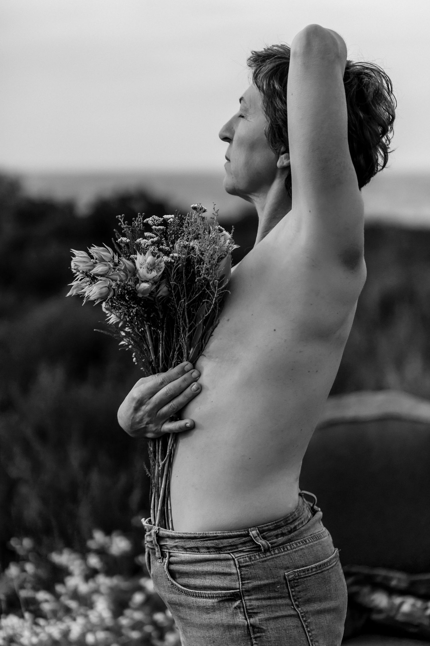 Black and white photographs show a figure in jeans standing against nature, holding wildflowers with arms raised.