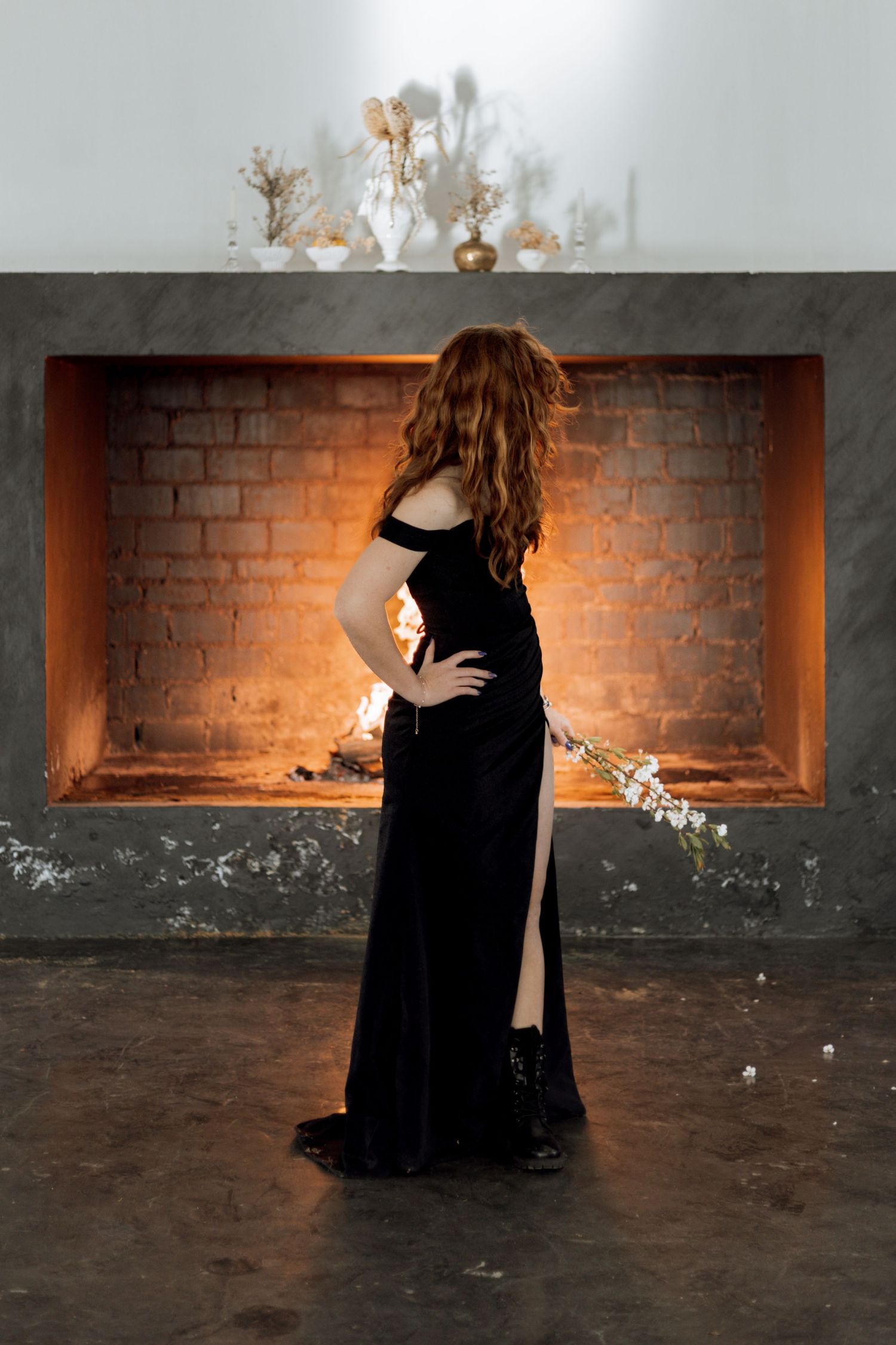 A silhouette in an elegant black velvet gown poses in front of a brick-lined alcove filled with warm light.