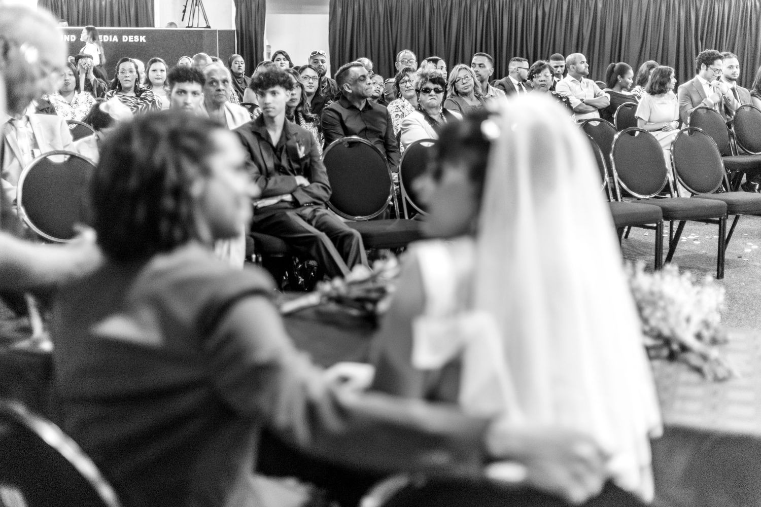 A wedding ceremony features audience members seated in rows watching the couple at the altar.
