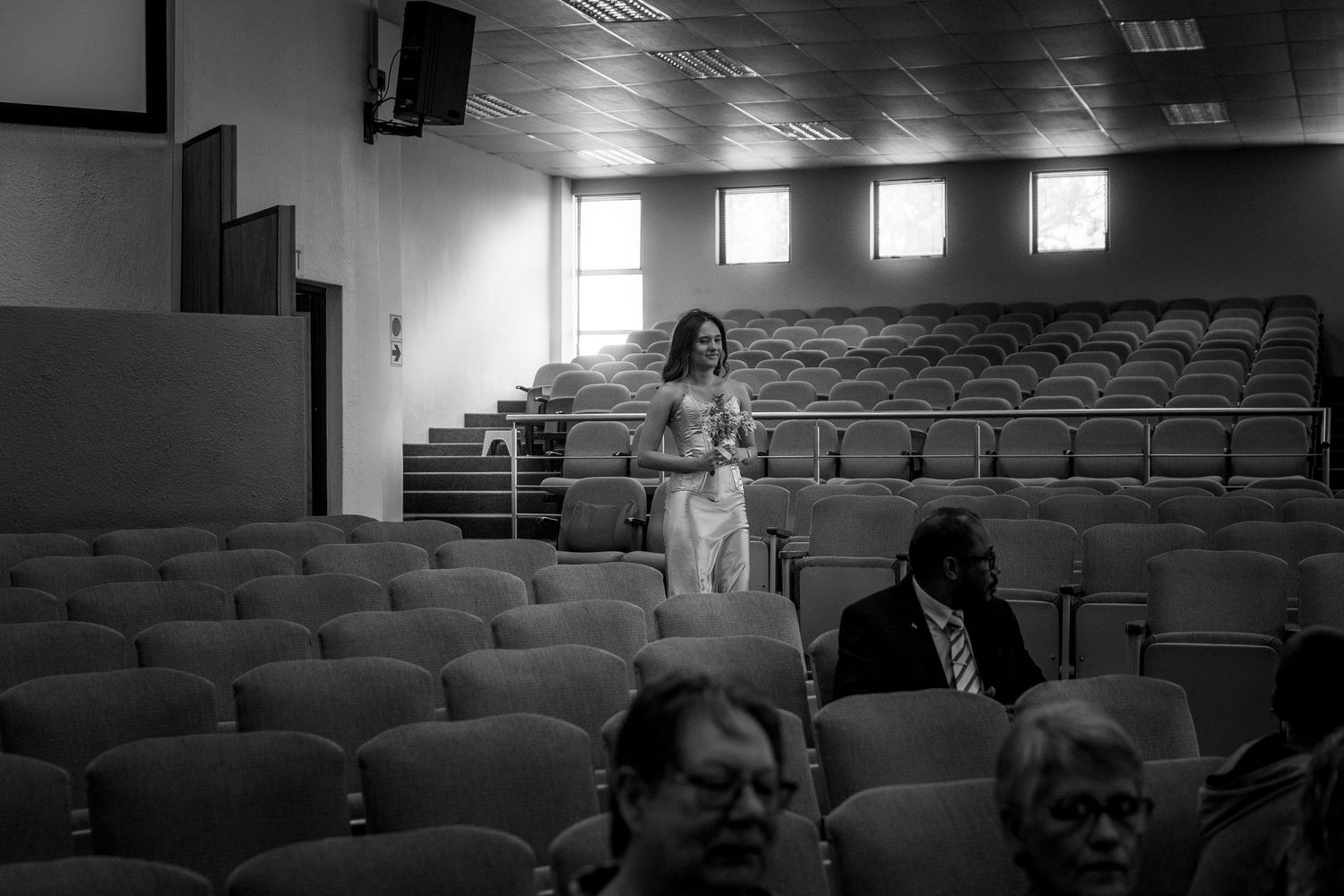 A black and white photograph shows people scattered across rows of seats in a lecture hall or auditorium.
