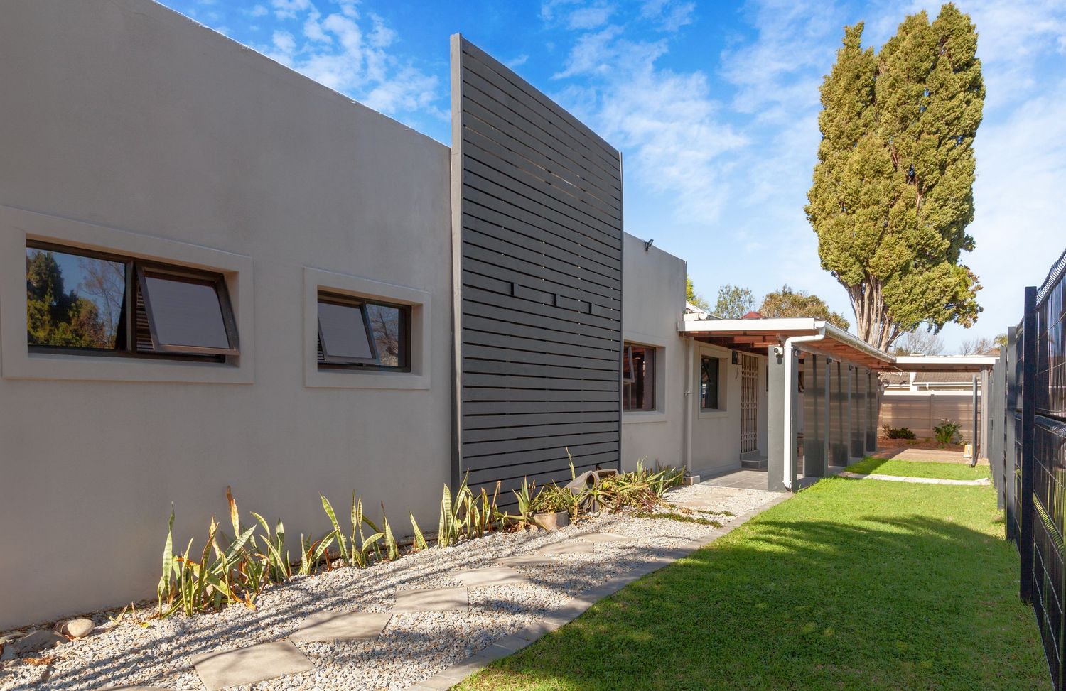 Modern residential building exterior with blue sky, cypress trees, and landscaped yard viewed from multiple angles.