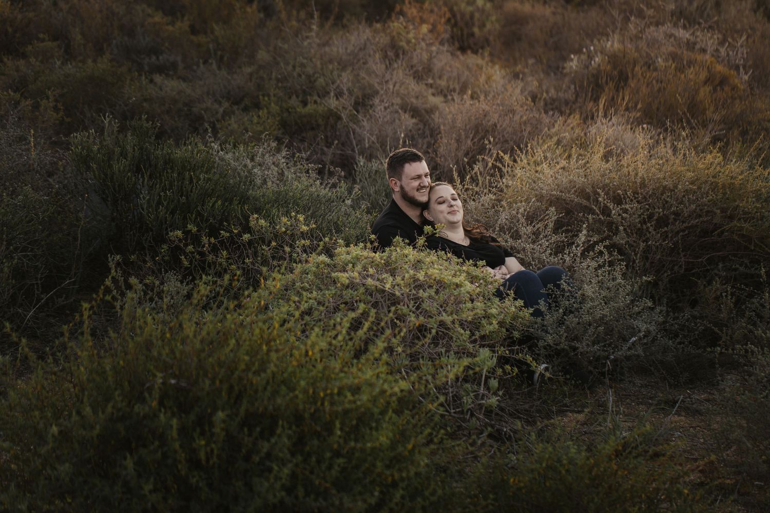 A person walks through a serene natural landscape with tall grass and bushes during golden hour lighting.