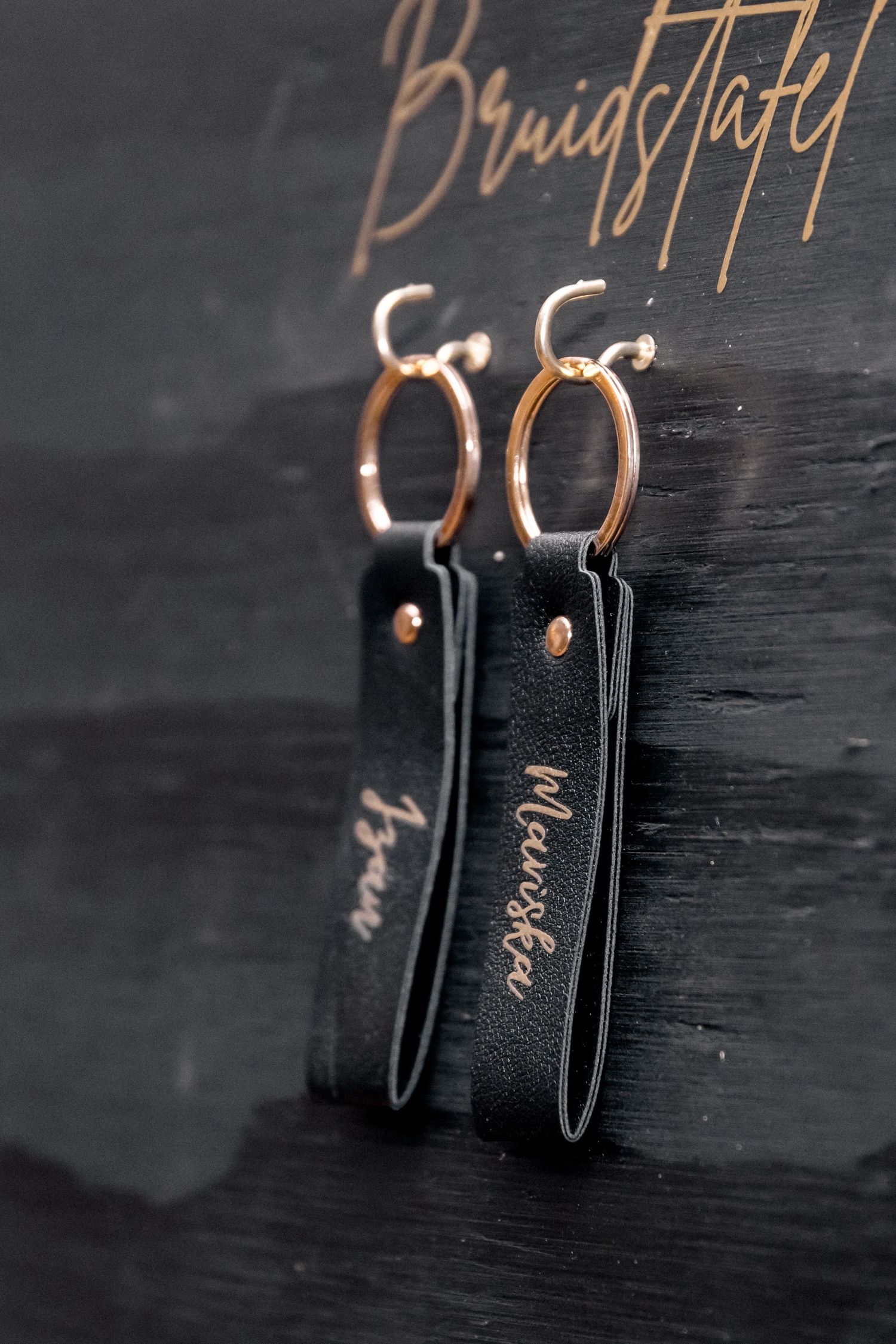 Close-up view of black leather earrings with copper wire hooks on a dark wooden surface.