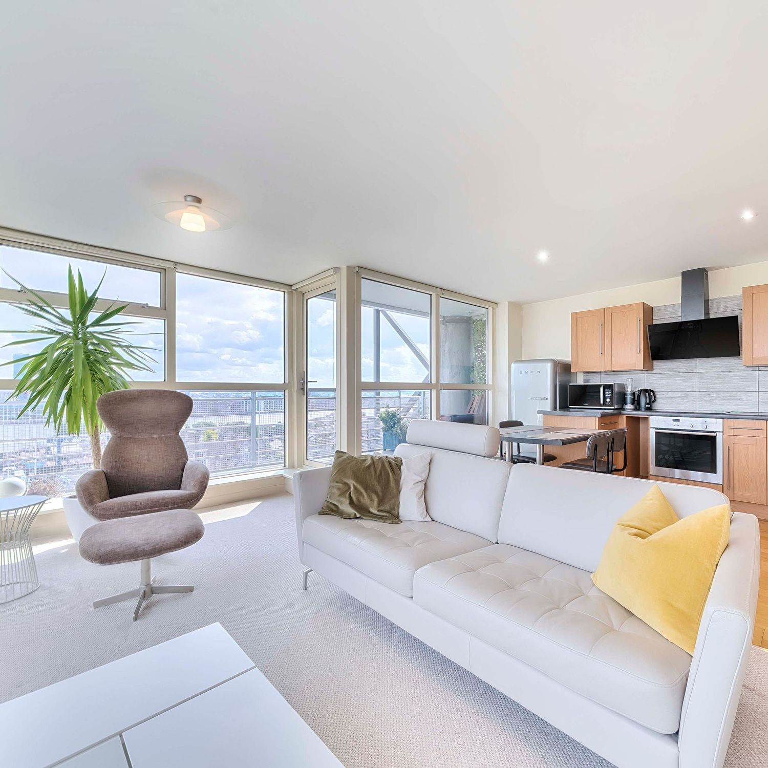 Modern apartment living room with floor-to-ceiling windows, white sofa, brown chair and city views.