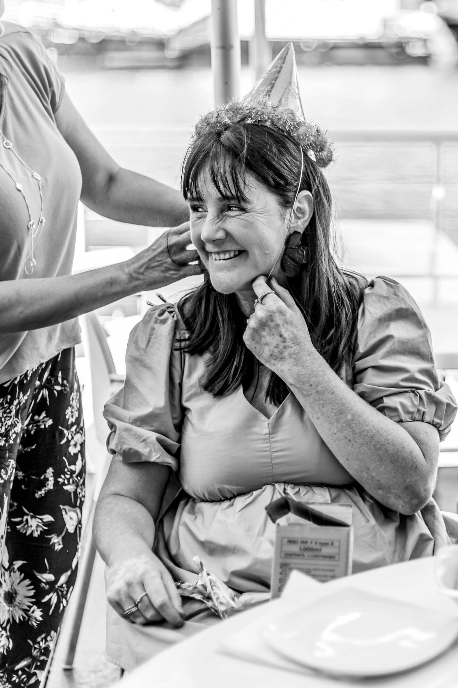 Black and white candid photograph of a birthday celebration showing someone wearing a party hat while smiling joyfully.