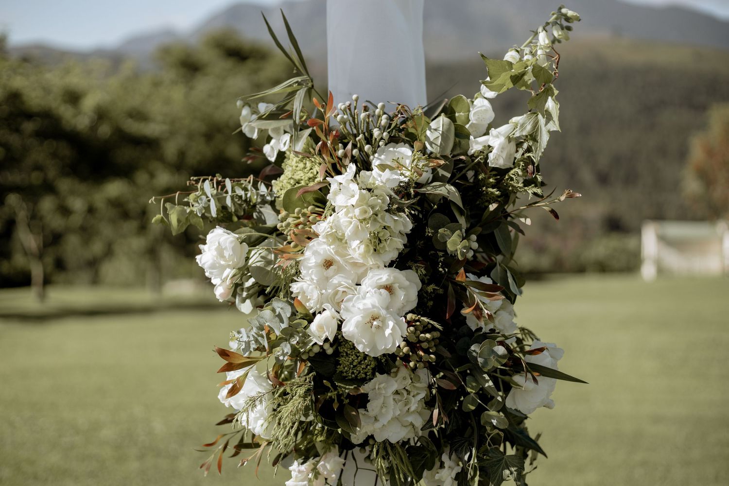 Elegant floral bouquets and wedding decorations against scenic mountain backdrop create a romantic outdoor ceremony setting.