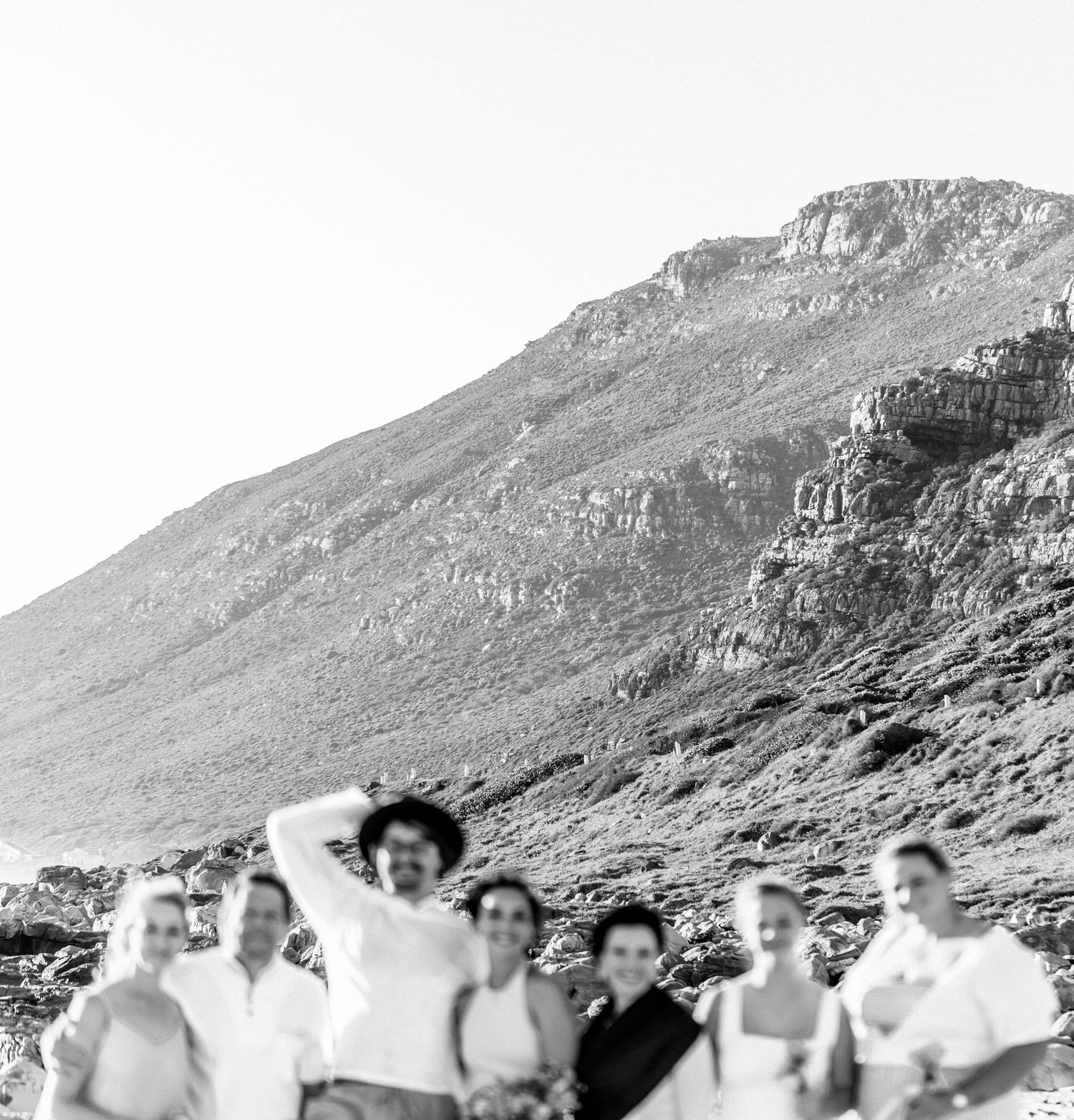 A vintage black and white photograph showing a group of people standing together at the base of a rocky mountain slope.